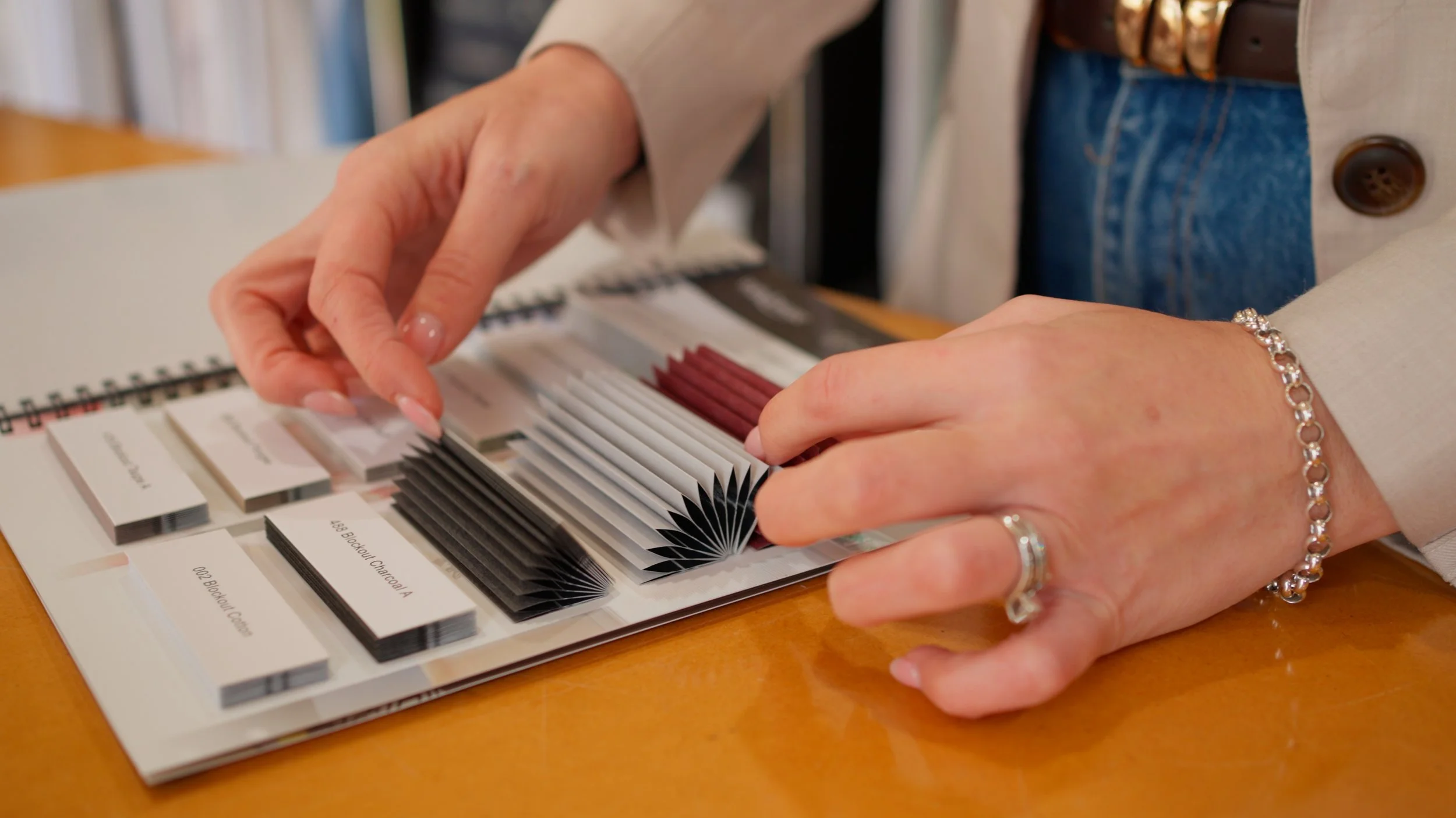 Person holding color swatch fan deck, selecting a shade, on a wooden table.