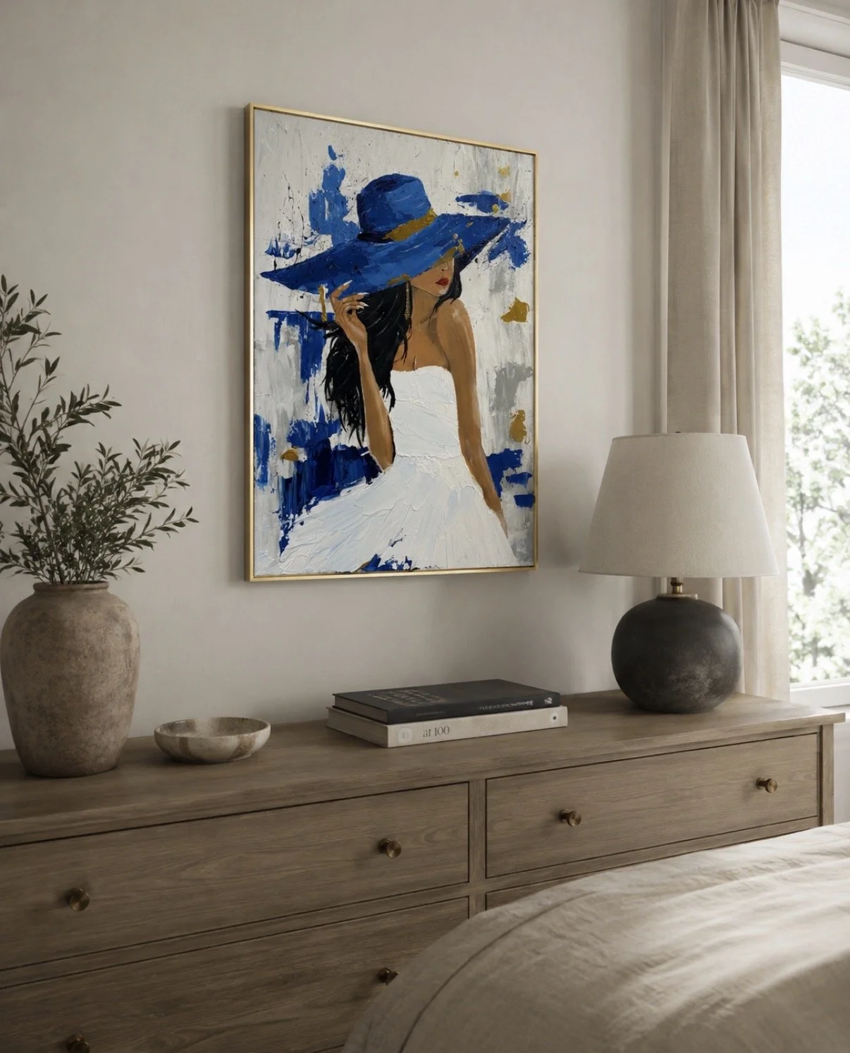 A bedroom with a wooden dresser, a large painting of a woman with a big blue hat, a potted plant, a stack of books, and a table lamp, near a window with beige curtains.