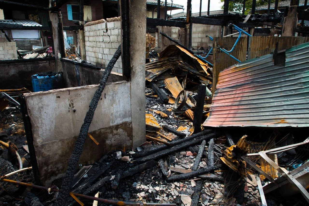 Burned remains of a building, with charred debris, broken metal sheets, and burned wooden beams.