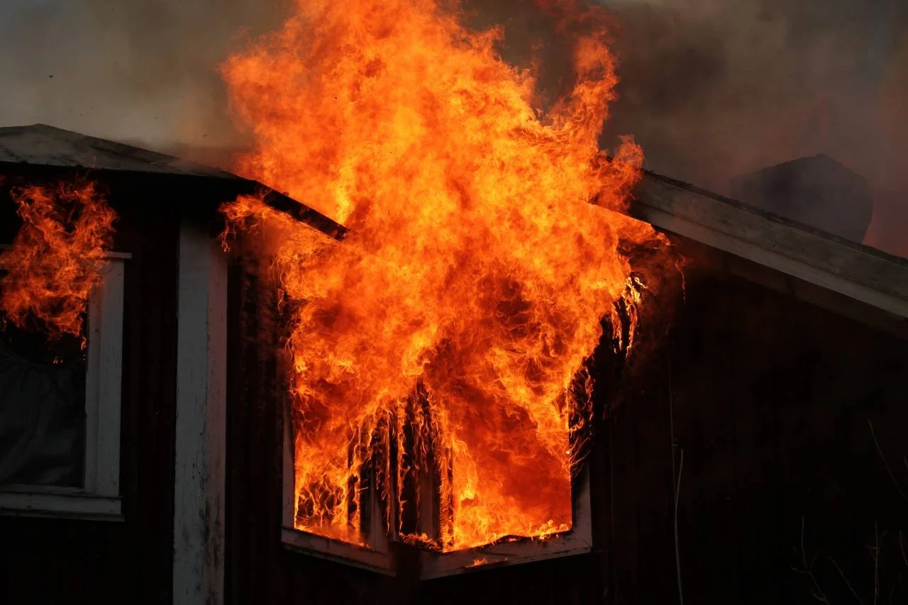 A house on fire with large flames erupting from the windows and roof.