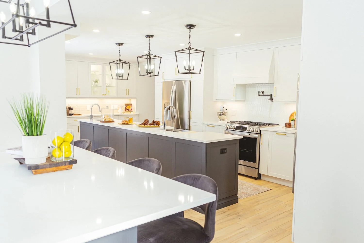 Modern kitchen with white cabinets, a large island with dark gray finish, stainless steel refrigerator, and pendant lighting.