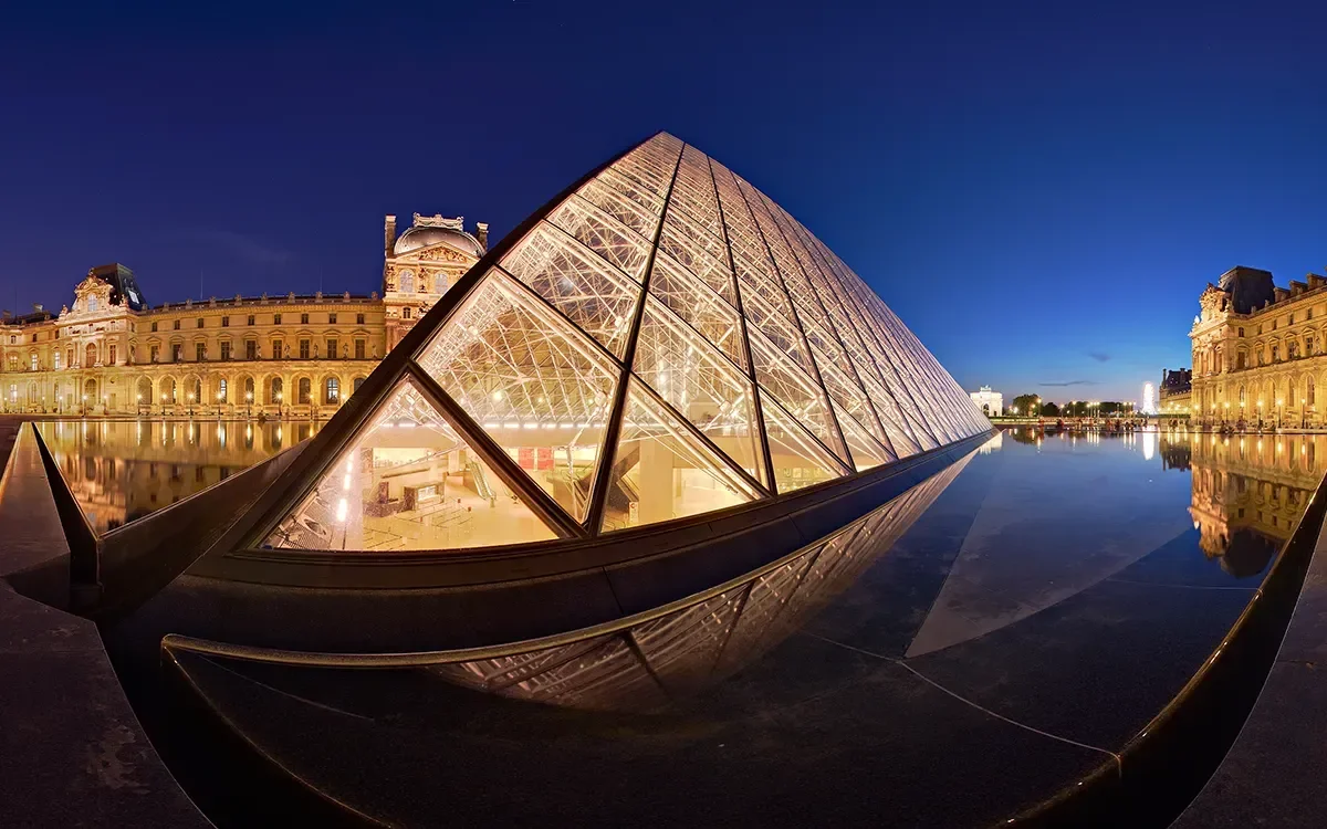 Panoramic evening view of the Louvre Museum in Paris, France, representing ImmerseMe's immersive French language learning experiences inspired by authentic French locations.