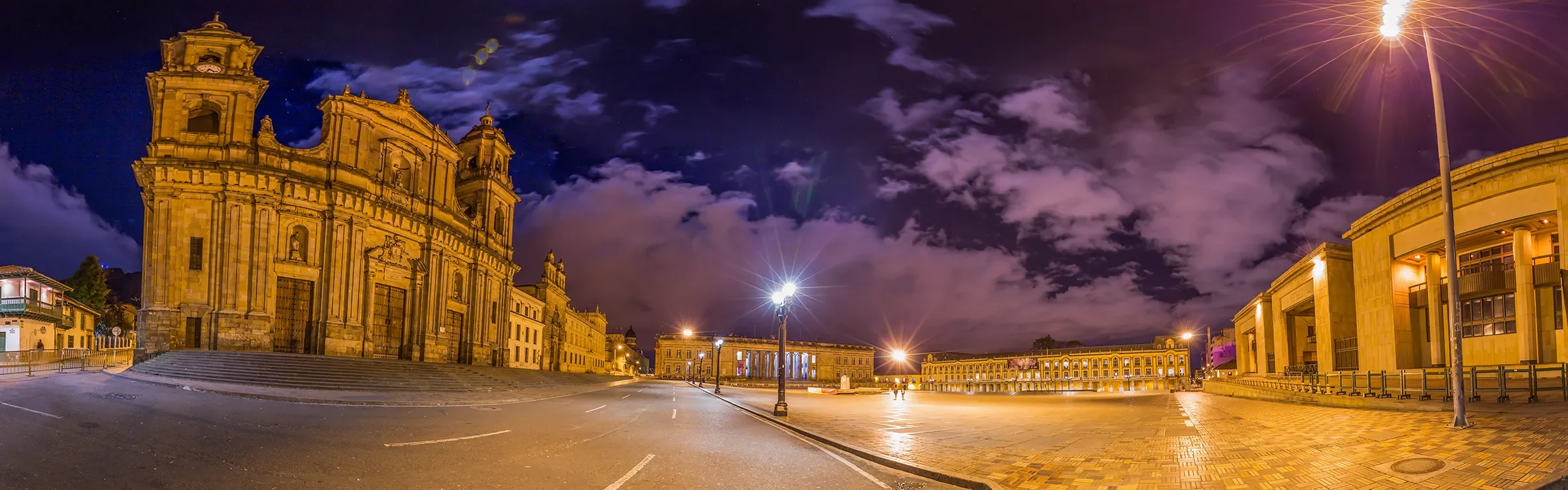 Plaza de Bolívar in Bogotá, Colombia at night, featuring the Primatial Cathedral and historic government buildings illuminated under a dramatic sky, representing Spanish language and Latin American culture.