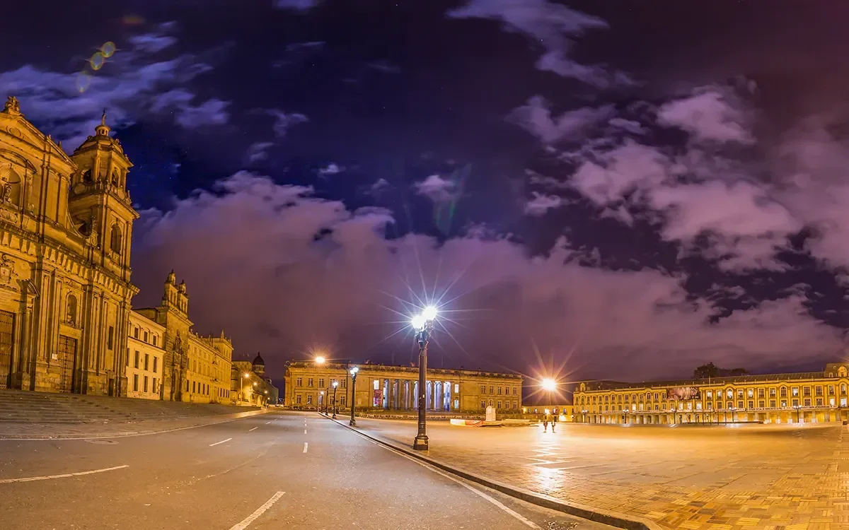 Plaza de Bolívar in Bogotá, Colombia at night, featuring the Primatial Cathedral and historic government buildings illuminated under a dramatic sky, representing Spanish language and Latin American culture.