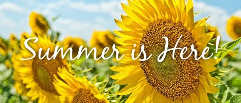 Close-up of bright yellow sunflowers in a field with a blue sky background and white clouds, with the overlay text 'Summer is Here!' in white cursive font.