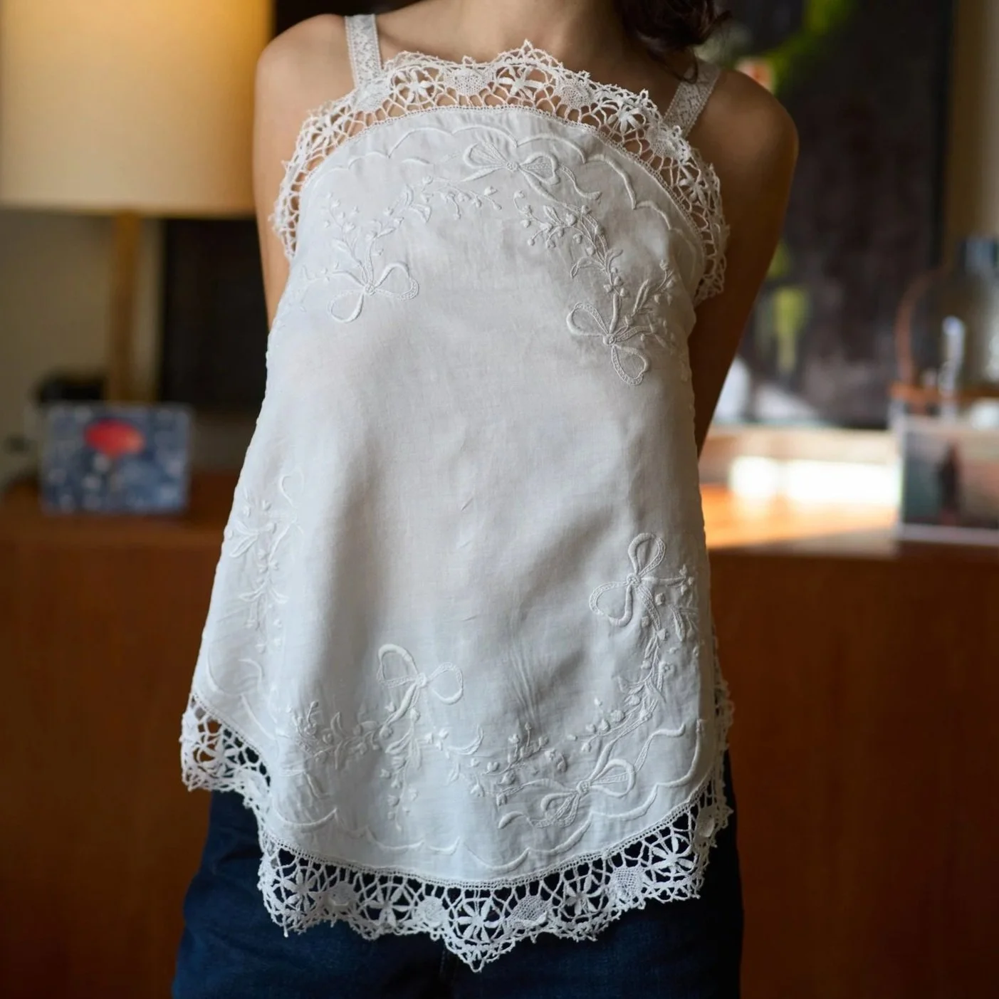 A woman wearing a sleeveless white embroidered top with lace details and scalloped edges.