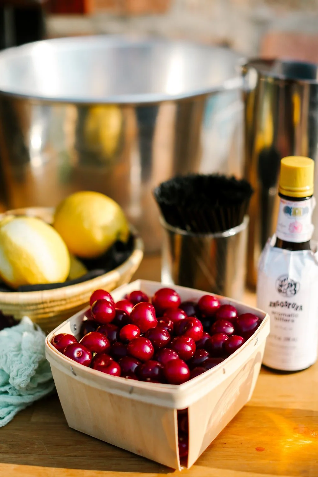 Basket of fresh red cherries, lemons, and various kitchen tools on a wooden surface.
