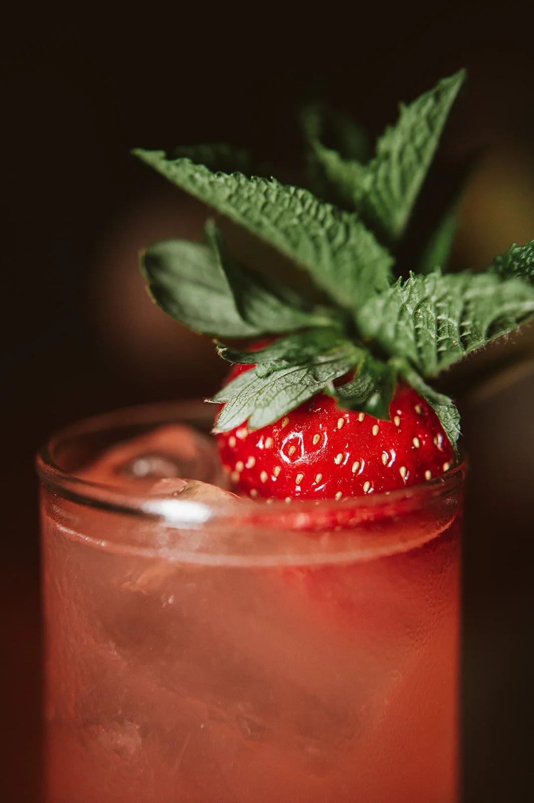 Close-up of a strawberry garnishing a pink beverage in a glass, topped with fresh mint leaves.