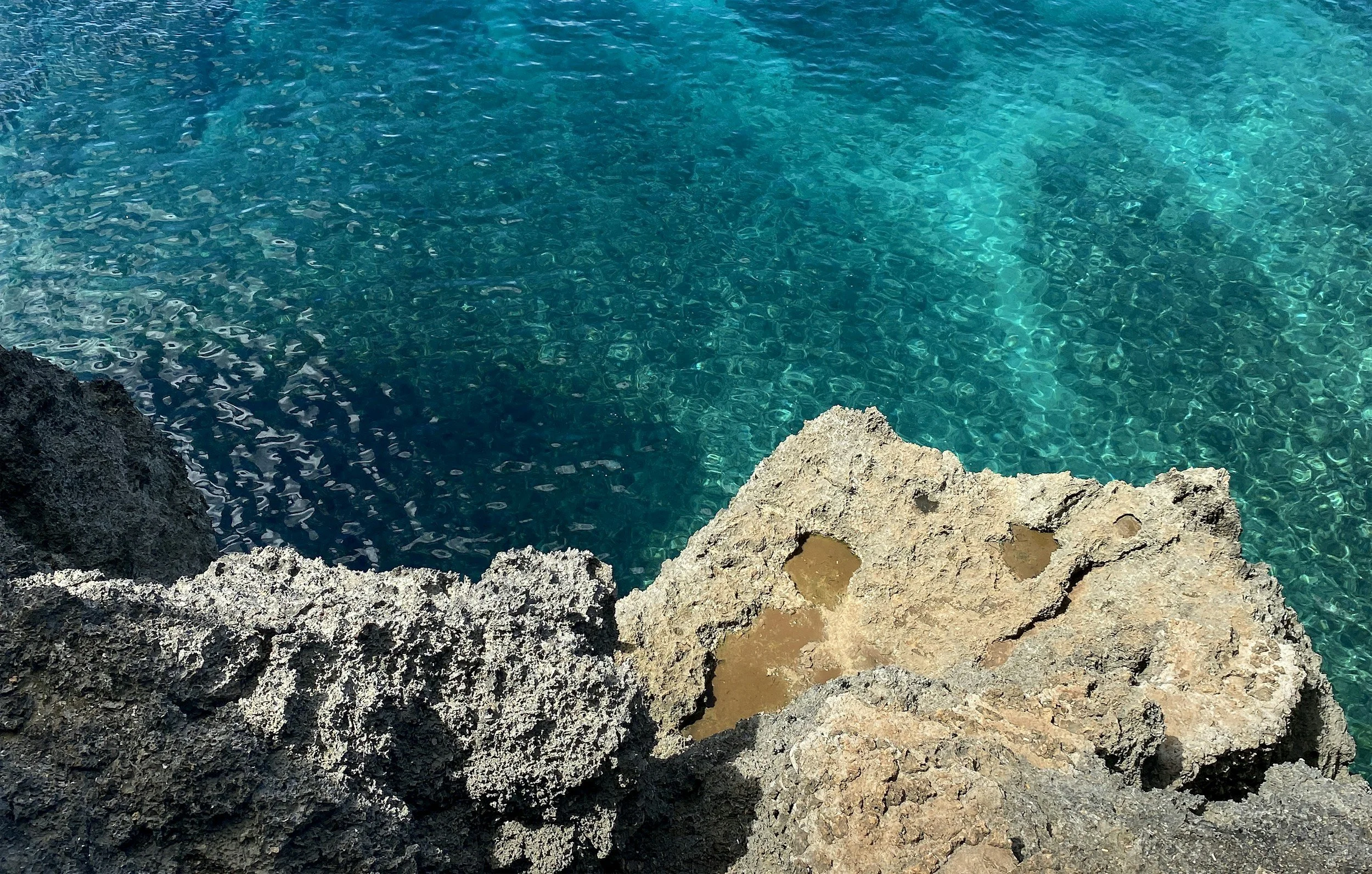 View of clear turquoise water near rocky shorelines with two large rocks protruding into the water.
