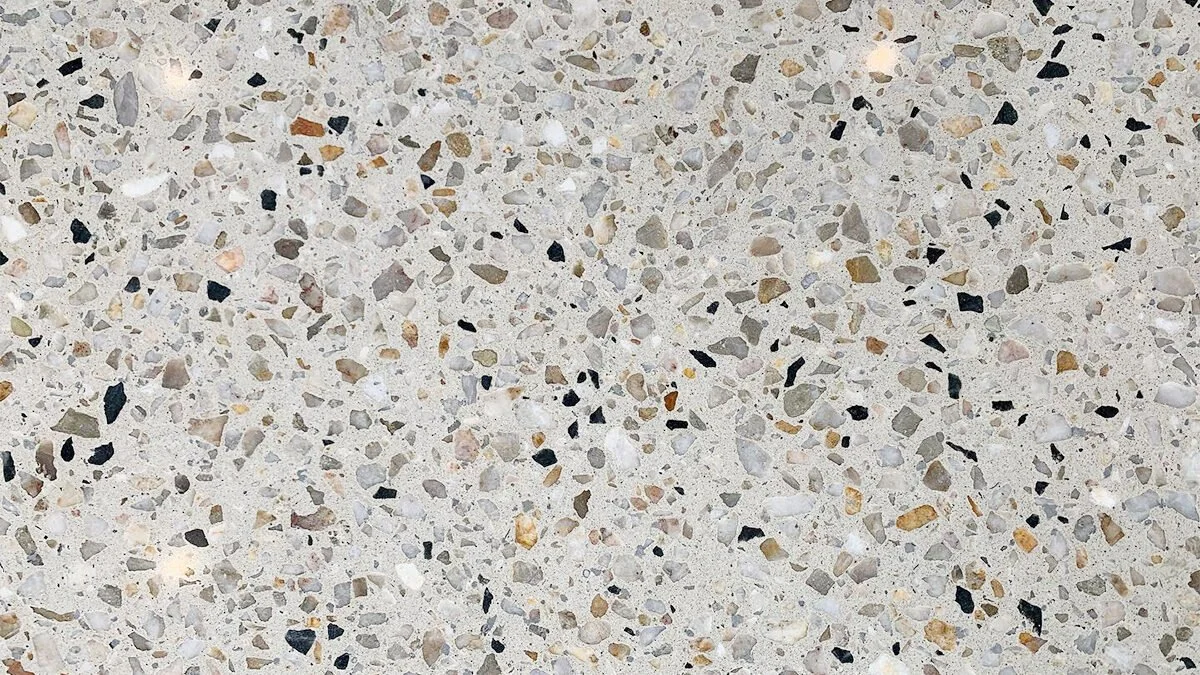 Close-up of a honed floor with a mixture of small, irregularly shaped stones in various colors, including black, white, gray, and tan, embedded in a light-colored cement base.