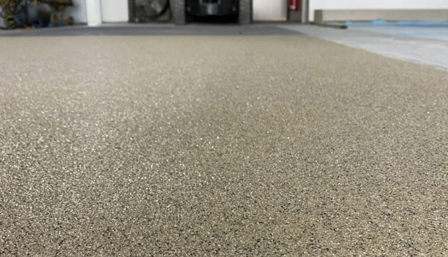 Close-up of a floor in a garage with some shelves and boxes in the background.
