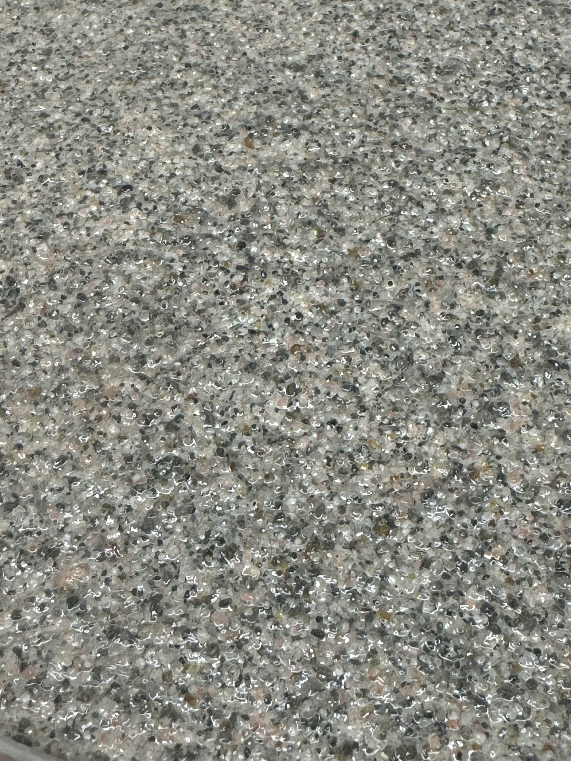 Close-up of a textured surface, with a mixture of small, shiny, gray and black particles.