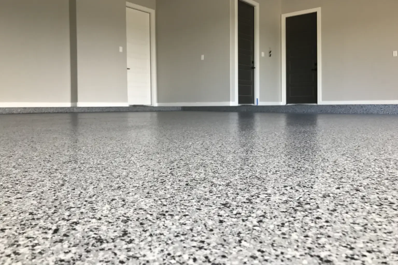 Indoor room with polished speckled gray flooring and three closed doors, two black and one white, on gray walls.