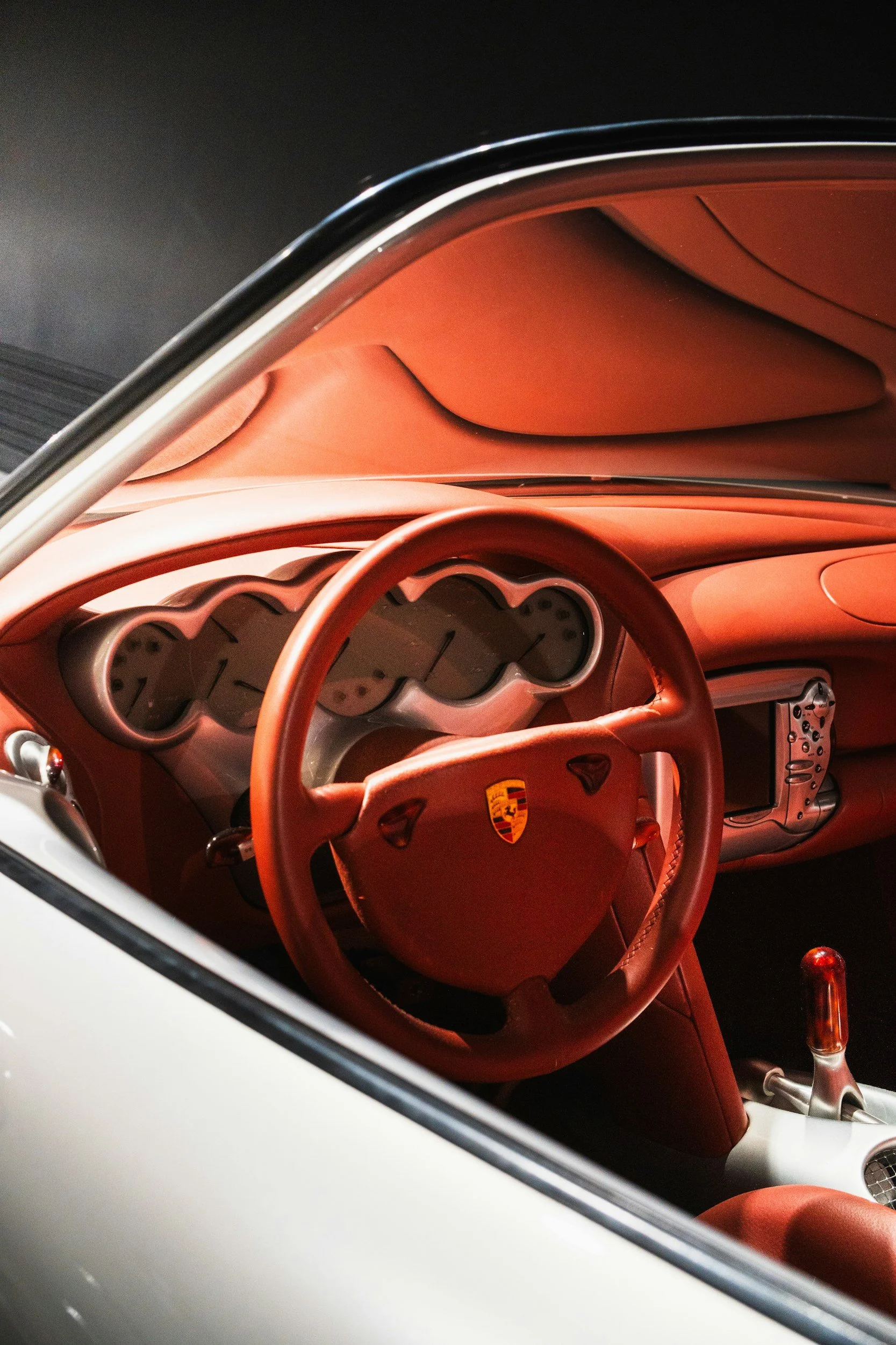Close-up of the interior of a luxury Porsche car, featuring a red leather dashboard, steering wheel, and gear shift, viewed through the window of a white car.