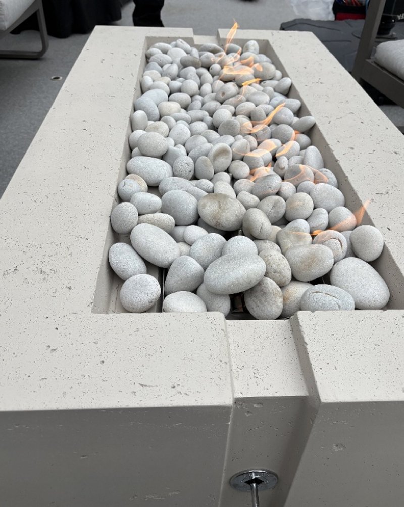 A rectangular fire pit filled with smooth white stones and small flames.