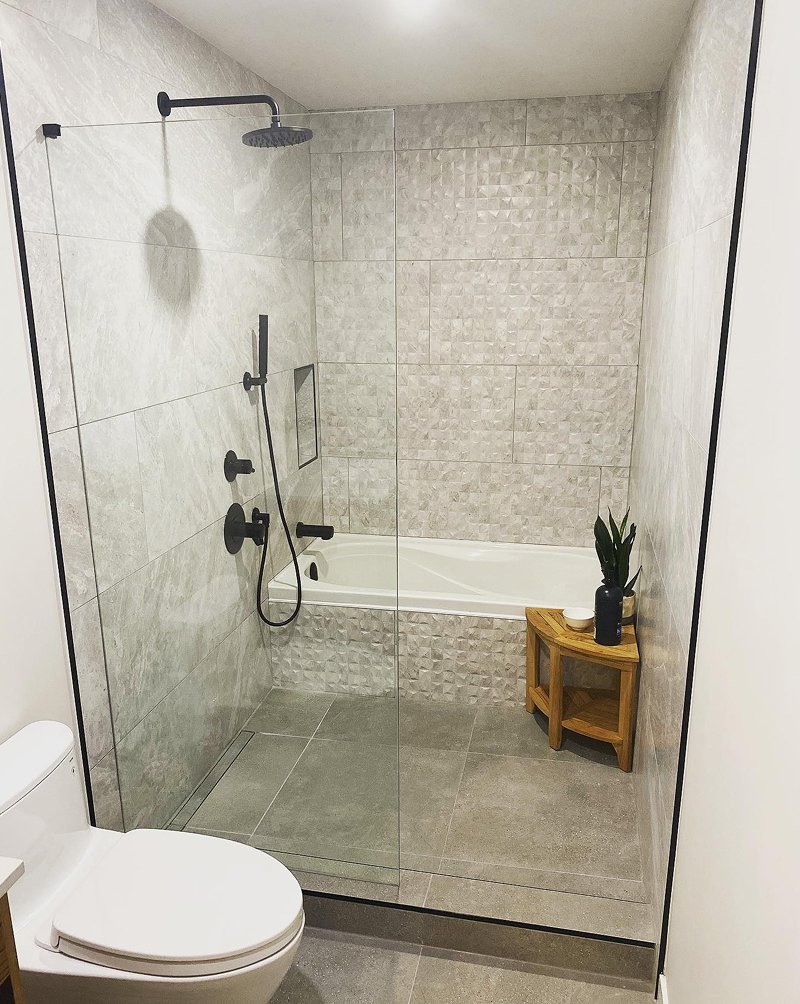 Modern bathroom with a walk-in shower with glass partition, a bathtub, and a small wooden side table with plants and decor.