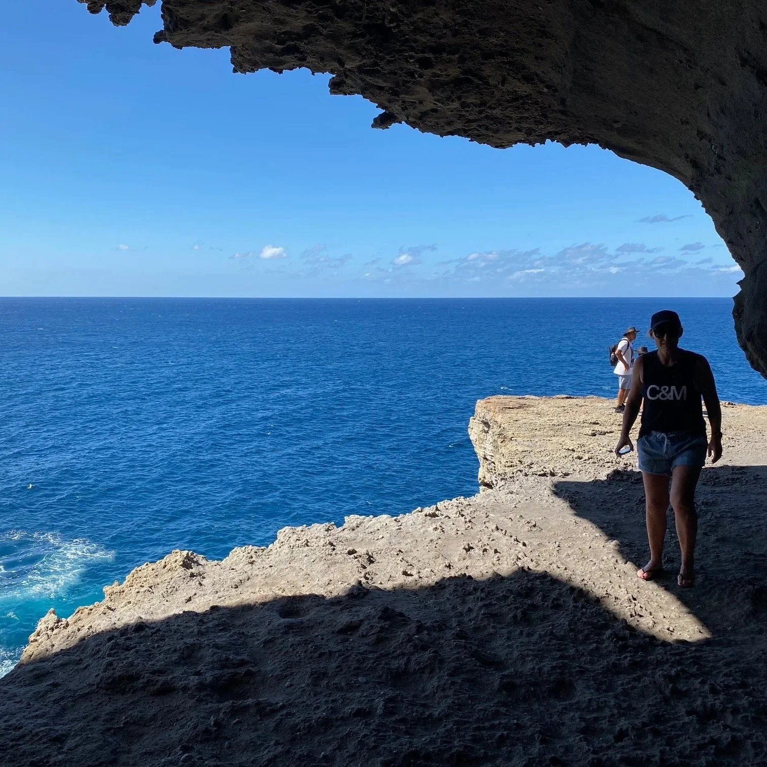 People exploring a rocky Gosangs Tunnel cave overlooking a vast blue ocean with on the Beecroft Peninsula.