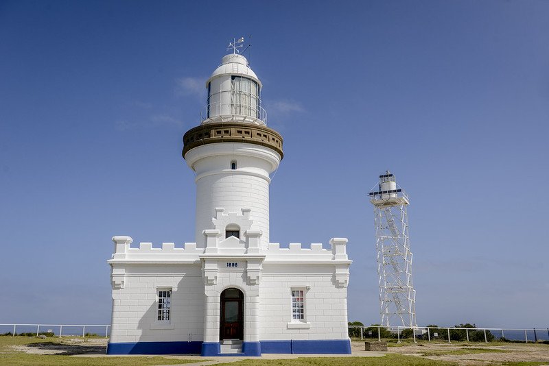The white Point Perpendicular lighthouse, situated on a grassy area with a clear blue sky in the background.