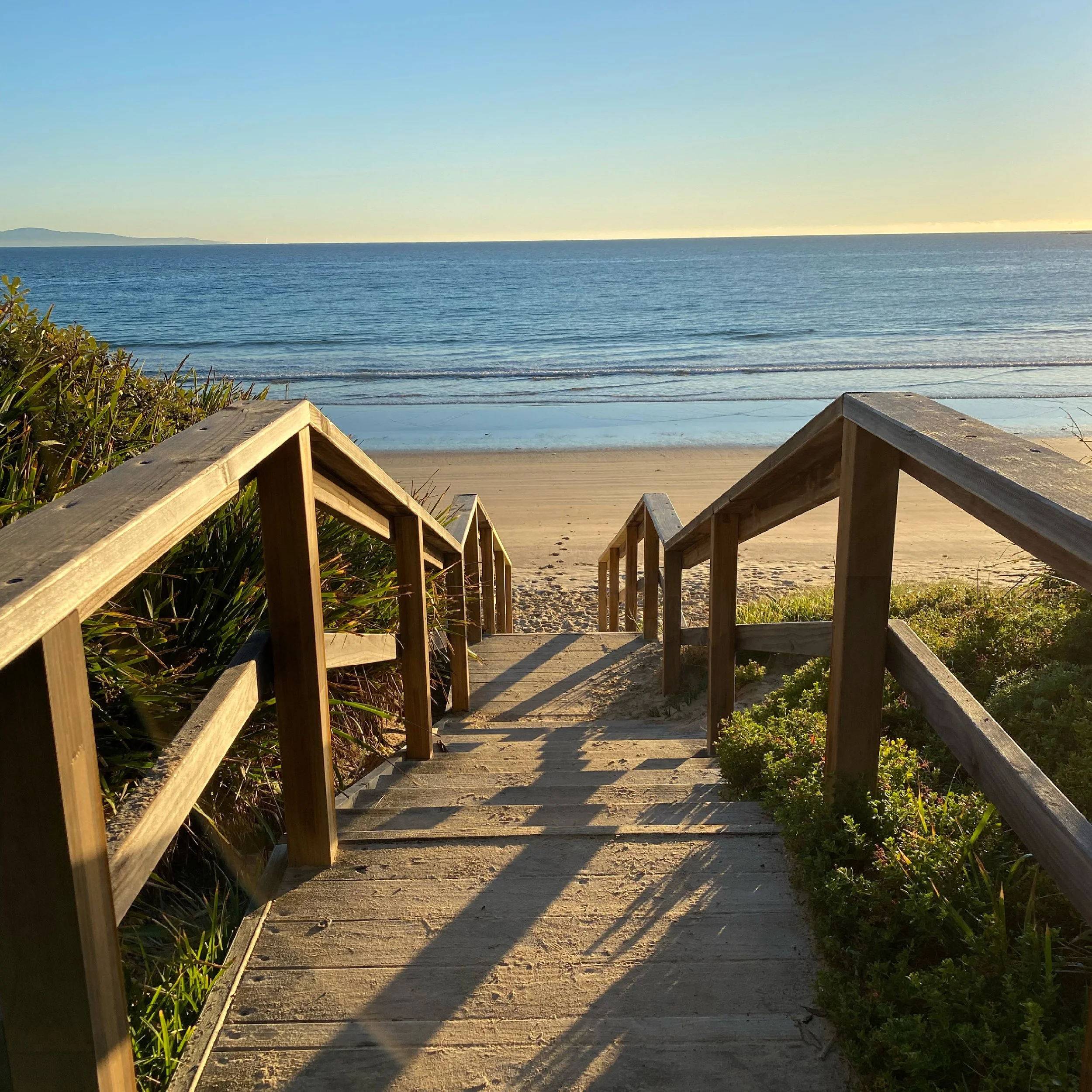 Wooden stairs leading down to the beach with sand and ocean waters visible and Culburra on the horizon.