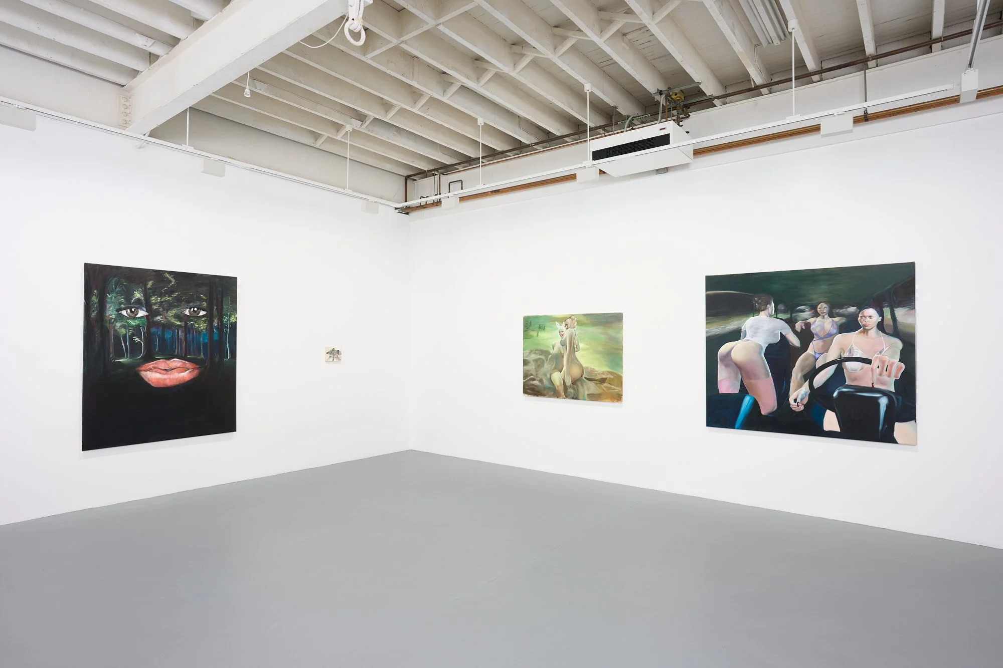 Photo of an art gallery with white walls and three paintings. The left painting features a face with large eyes and lips with dark, green, and blue tones. The middle painting depicts a seated dog with a woman in the background, set outdoors. The righ