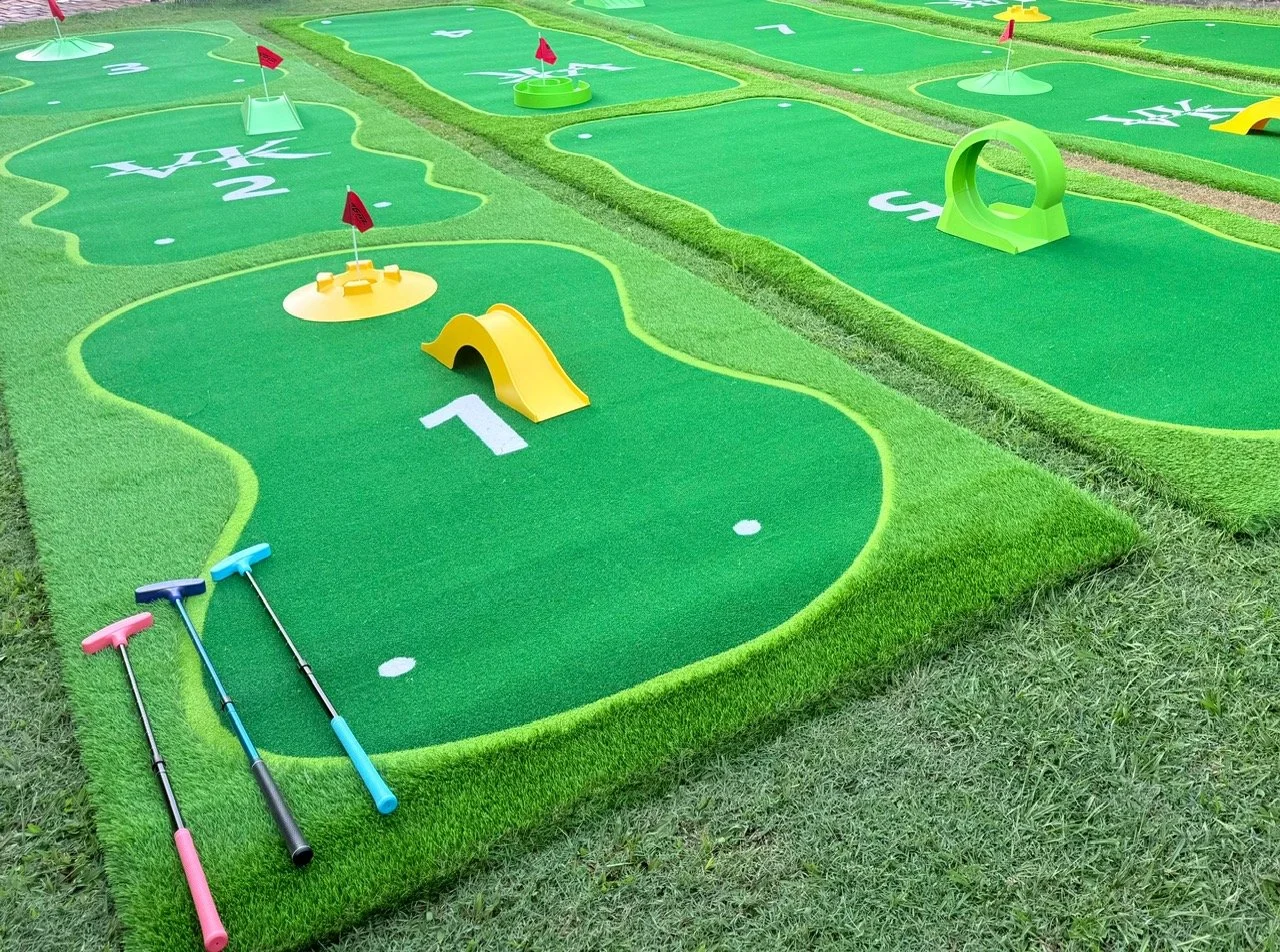 Miniature golf course with themed holes, including a yellow slide trap, flags, and golf clubs on green artificial turf.