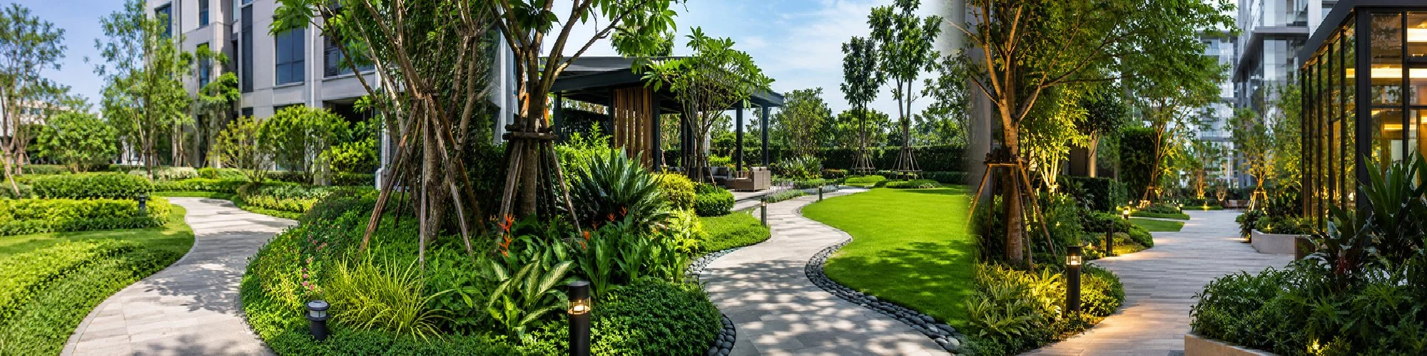 A landscaped outdoor garden area near modern residential or commercial buildings, featuring pathways, lush green plants, trees, and outdoor lighting.