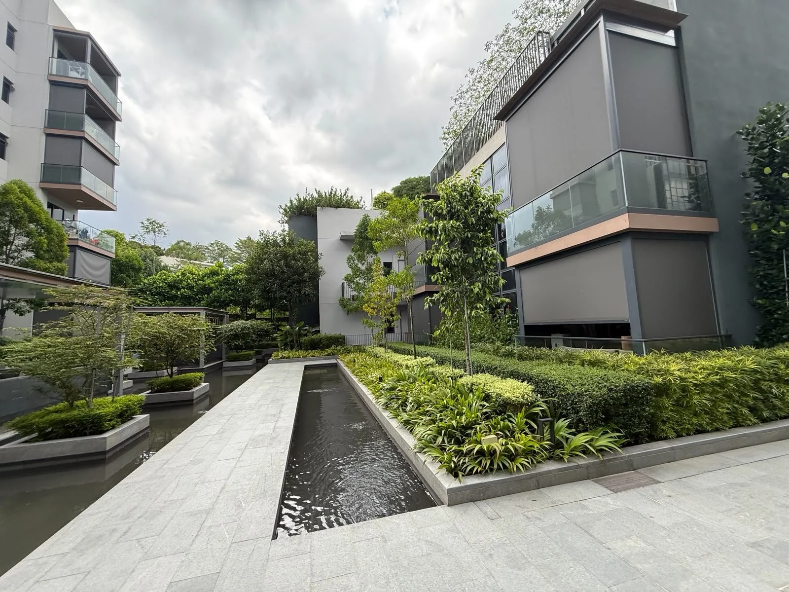 Modern apartment complex with landscaped garden and water feature, including a walkway and lush greenery.
