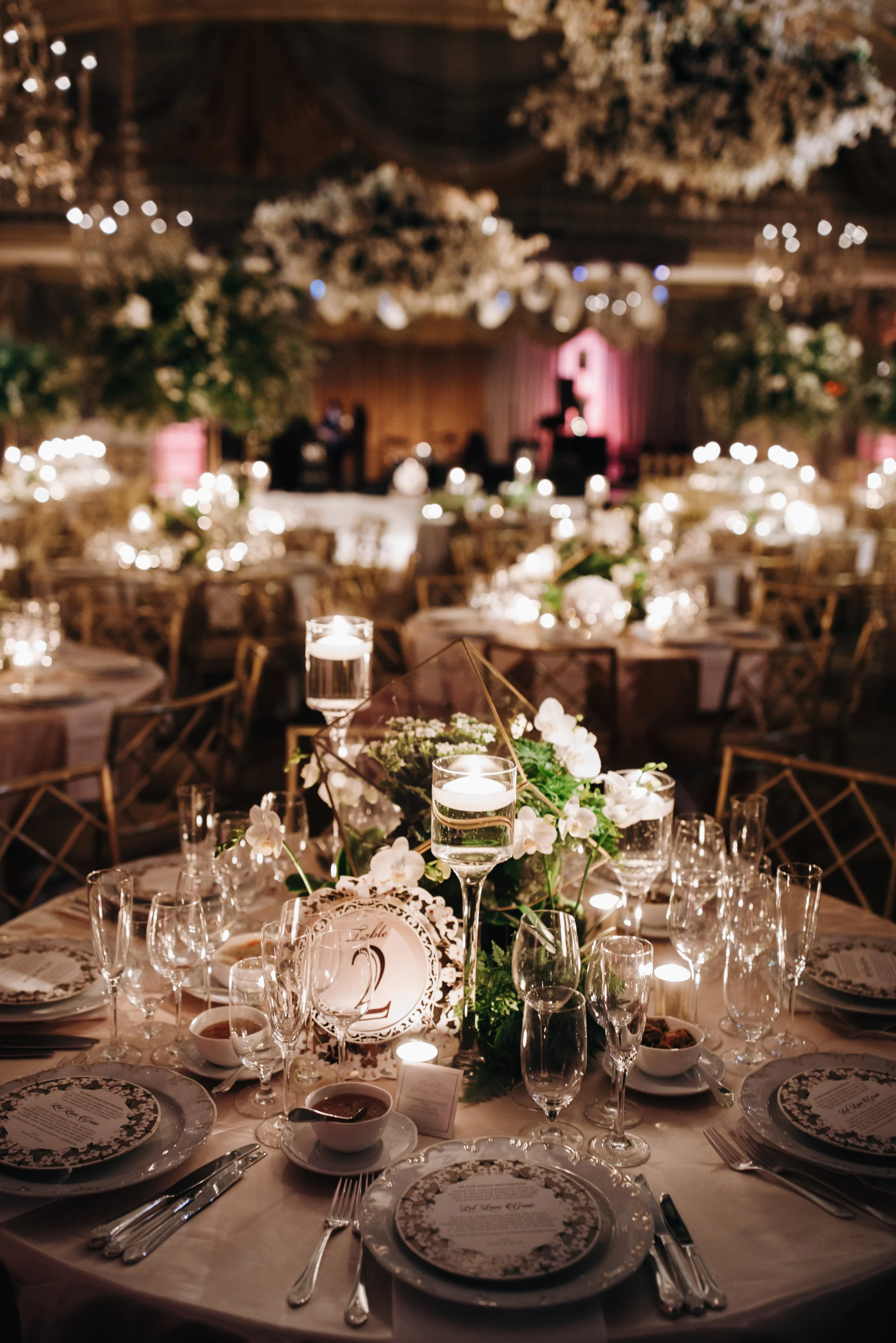 A banquet table set for a formal event with floral centerpieces, candles, dinnerware, and glassware in a decorated venue with dim lighting.