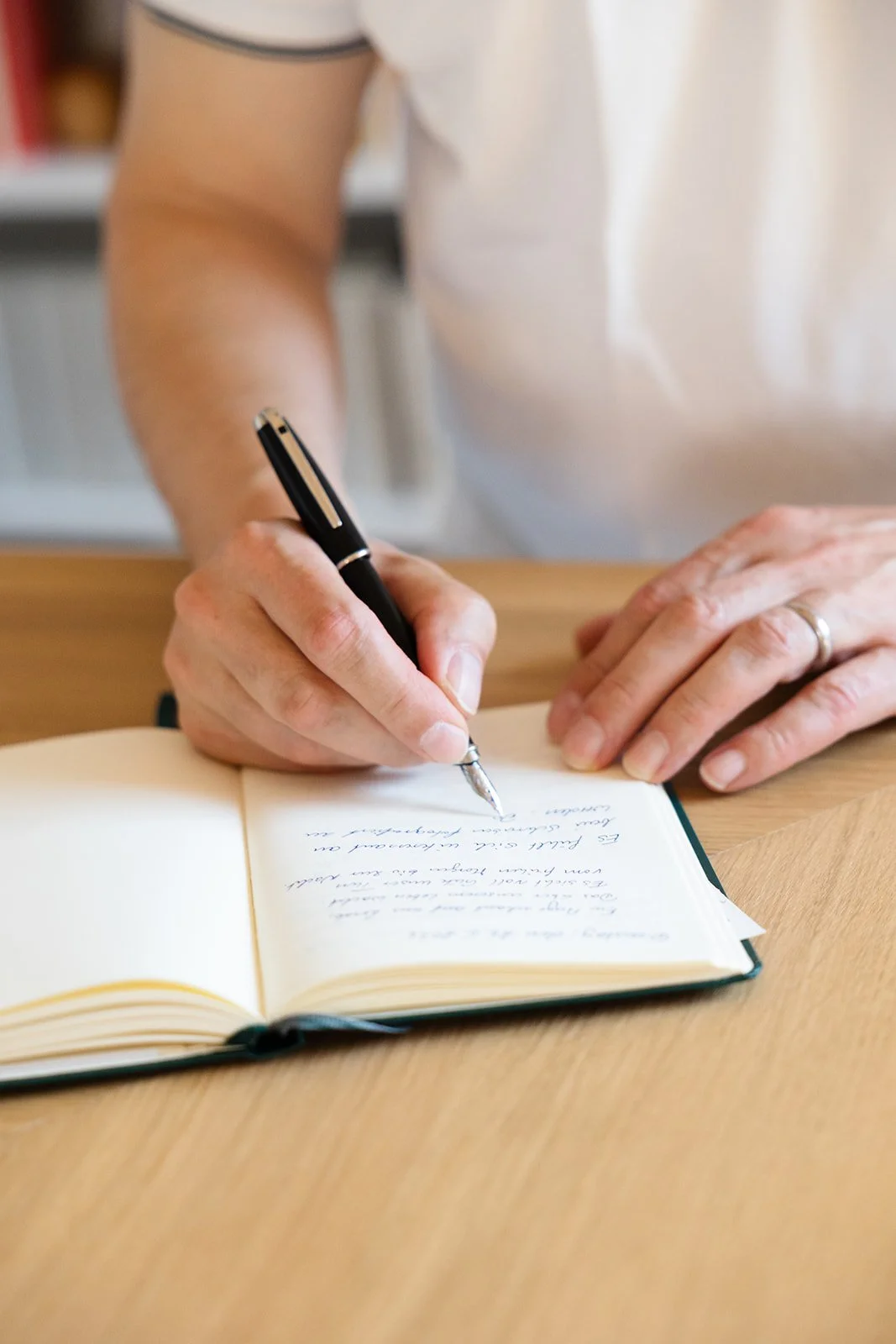 A person writing in a notebook with a black pen on a wooden table.