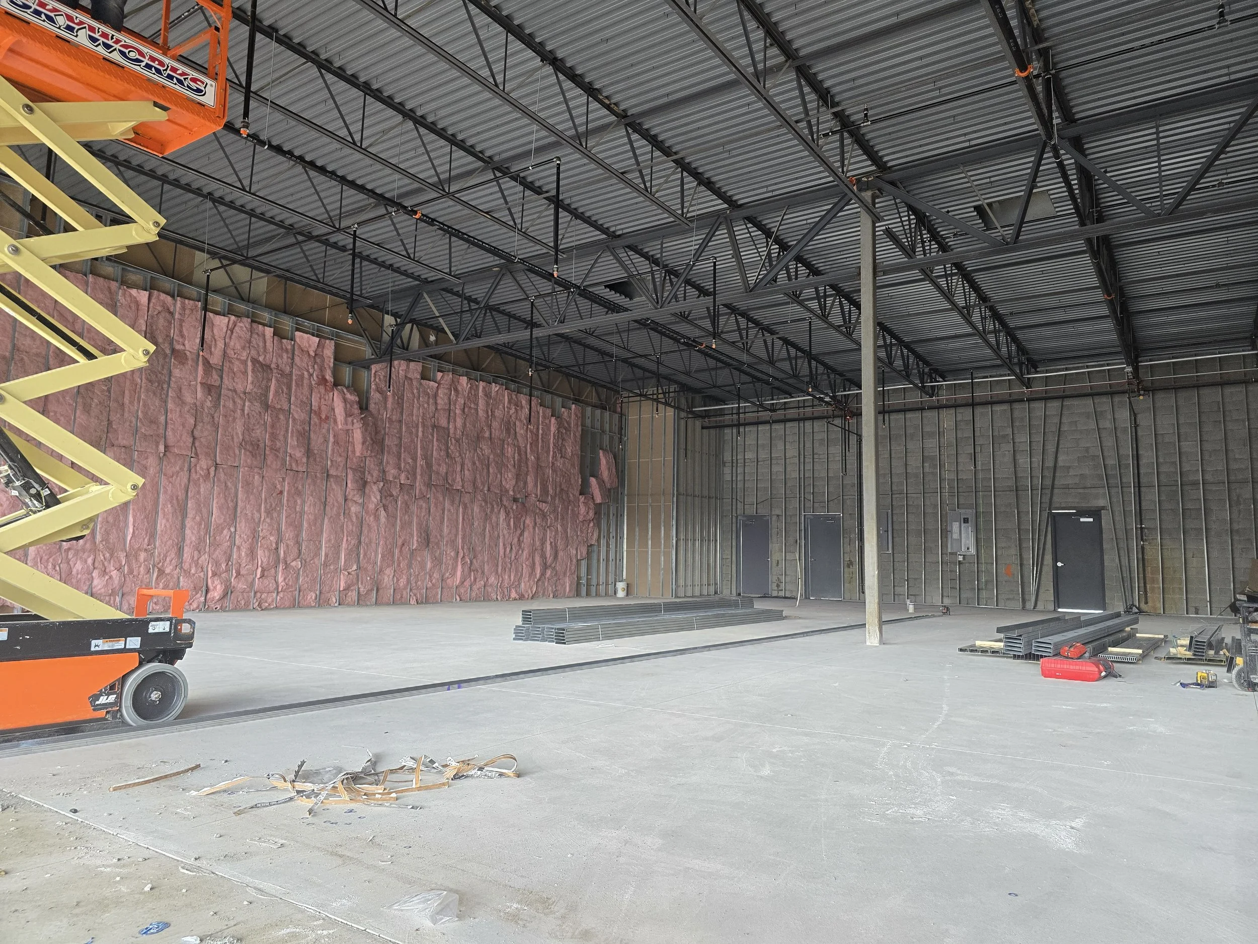 Construction site interior with steel beams, insulation panels, and construction tools and materials on the floor.