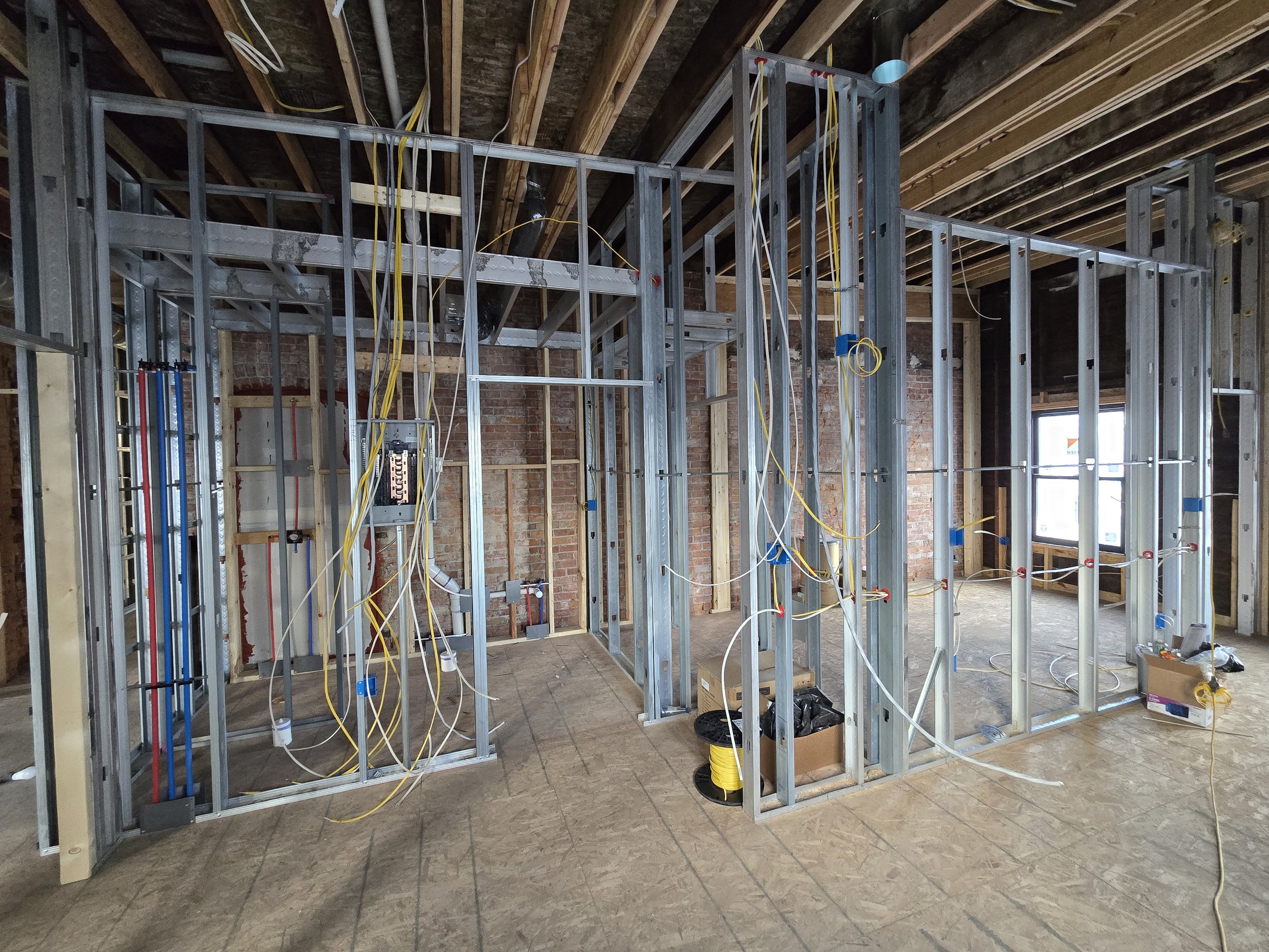 Interior of a building under construction with metal framing, exposed electrical wiring, and unfinished brick walls.