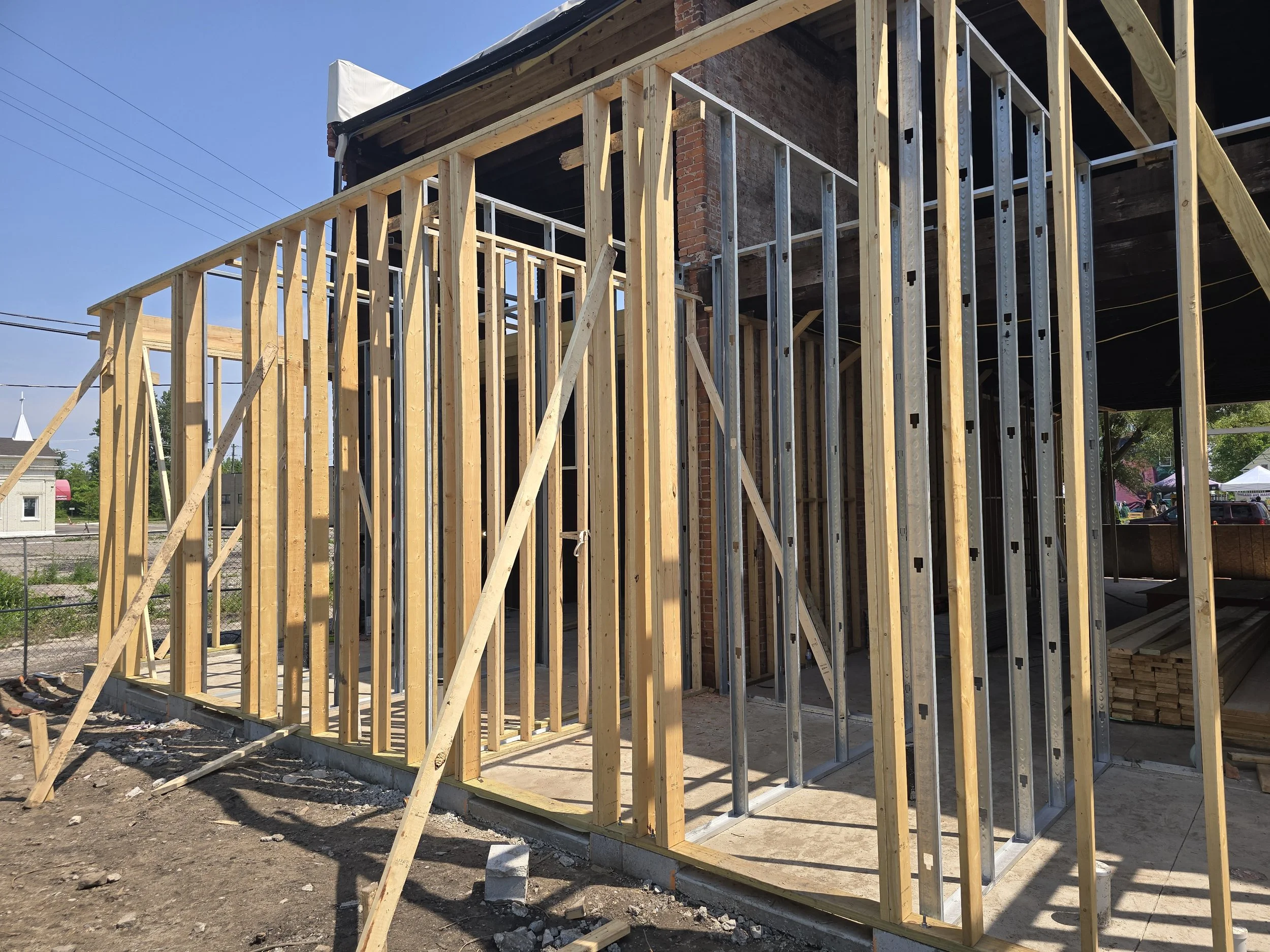 Wooden frame construction for a building in progress, with metal supports and a staircase, in a sunny outdoor setting.