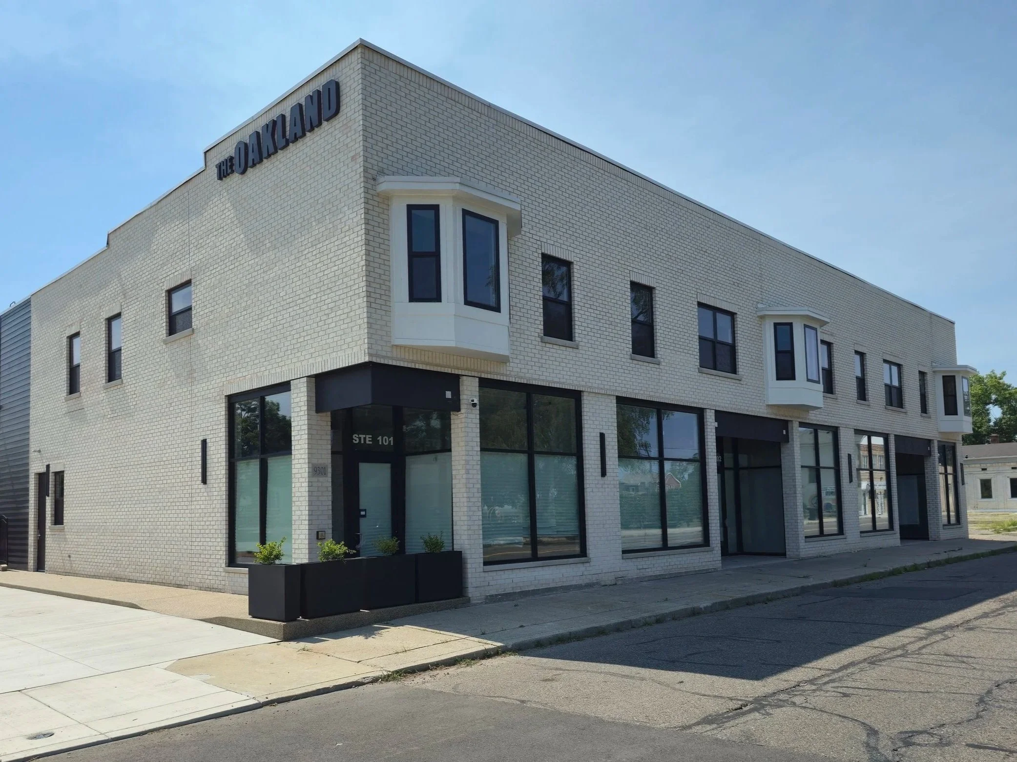 A modern, three-story building made of white bricks with large windows and black accents. The sign on the building reads 'The Oakland.'
