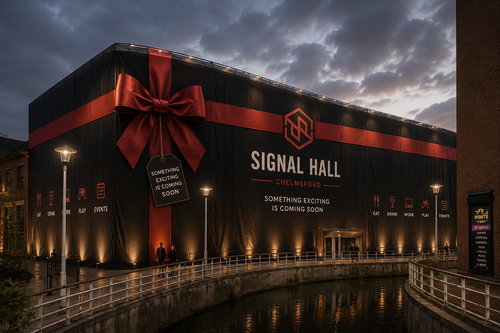 Signal Hall at Chelmsford decorated with a large red ribbon and bow, signage indicating upcoming events, and situated near a canal during dusk.