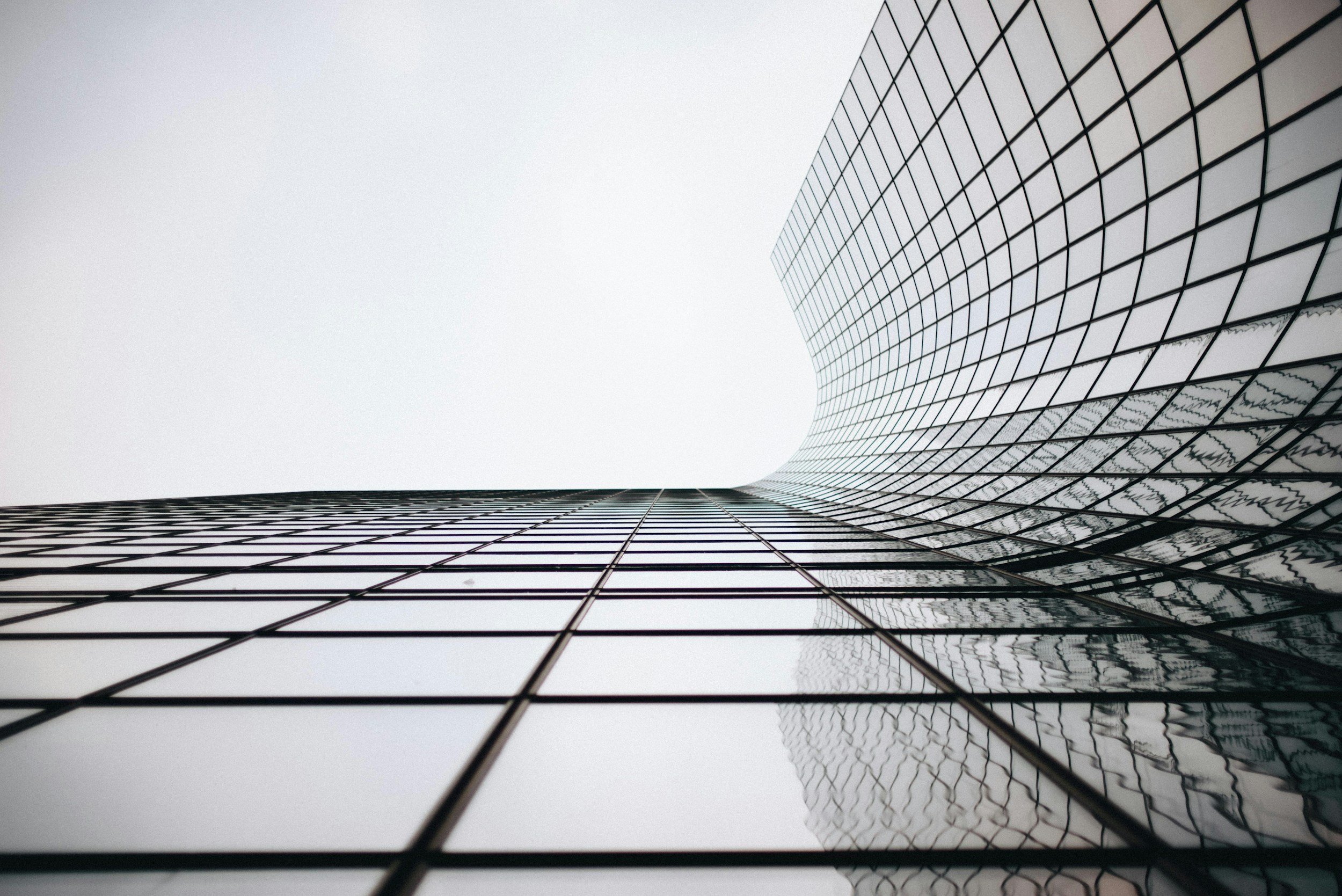 Low-angle view of a modern glass skyscraper with a curved facade against an overcast sky.