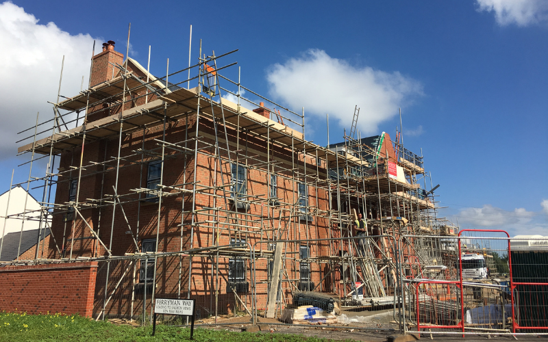 A brick building under construction with scaffolding surrounding it, workers on site, and a sign that reads 'Ferryway Way'.