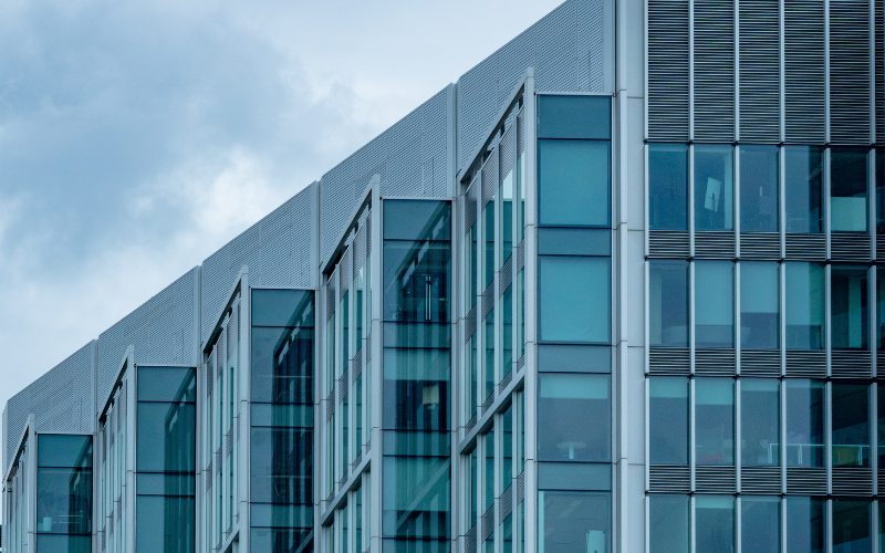 Close-up of a modern office building with glass windows and metal panels under a cloudy sky.