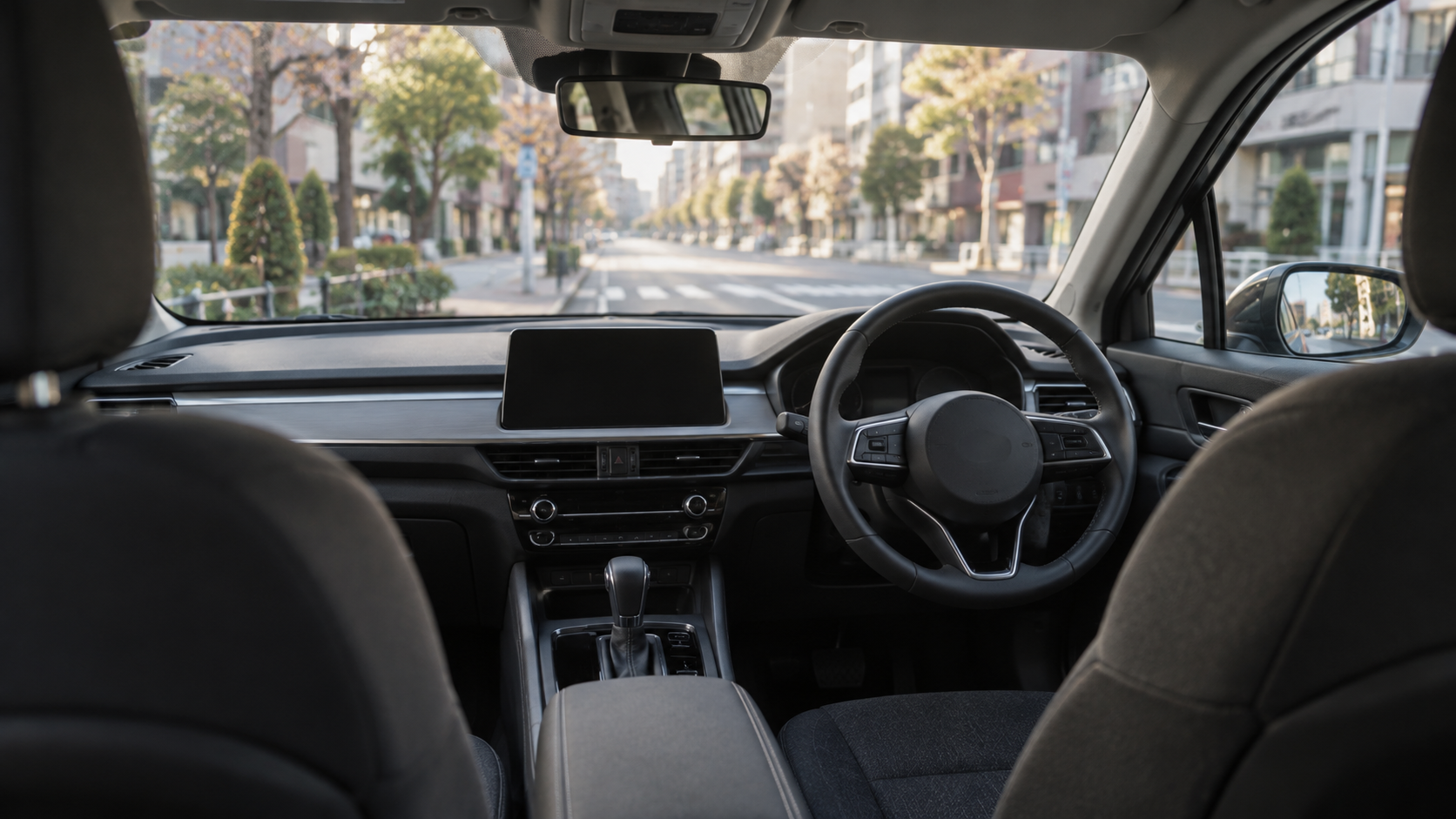 Empty front seats and a right-hand steering wheel inside an unbranded car overlooking a quiet Japanese city street.