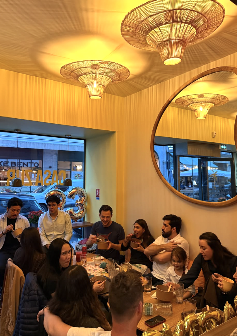 Grupo de personas celebrando en un restaurante con decoraciones de cumpleaños y globos dorados, comiendo y socializando.