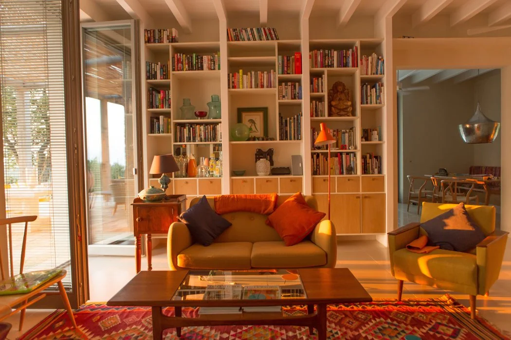 Living room with a beige couch and green armchair, coffee table, built-in white bookshelves, and glass sliding door with blinds.