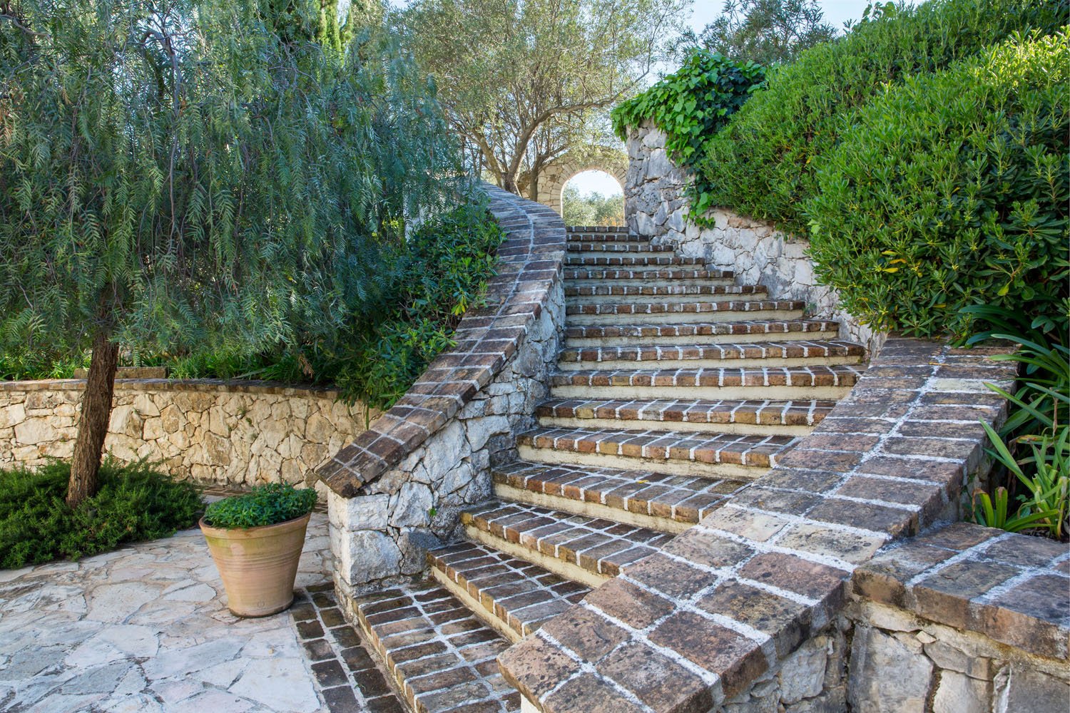 Stone and brick outdoor staircase surrounded by lush greenery and potted plants.