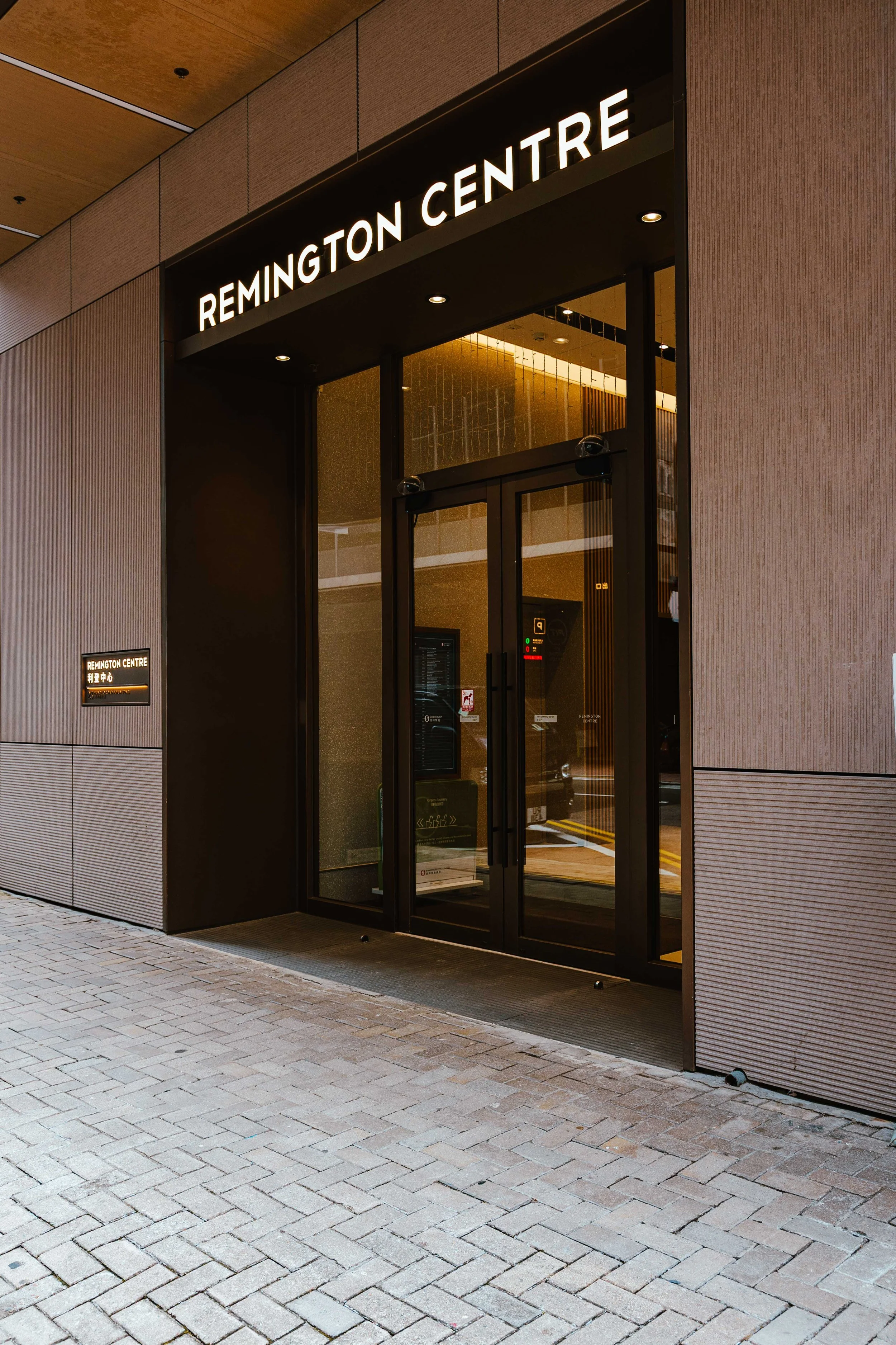 Exterior view of Remington Centre entrance with illuminated sign and glass doors, modern building facade, brick sidewalk in front.