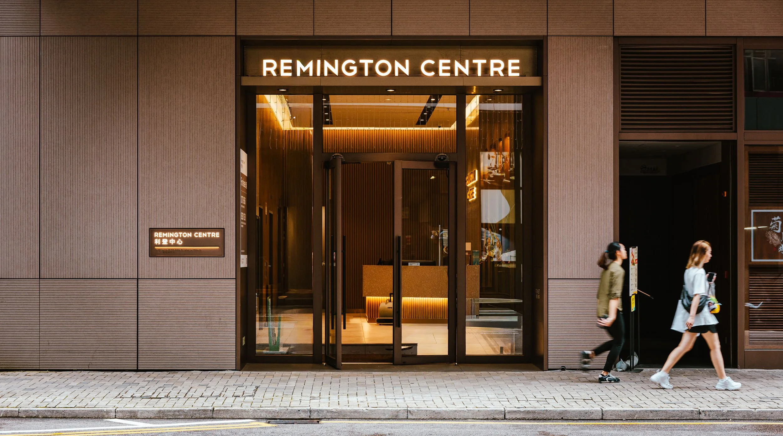 The entrance to Remington Centre shopping mall with a modern facade and two pedestrians walking by.