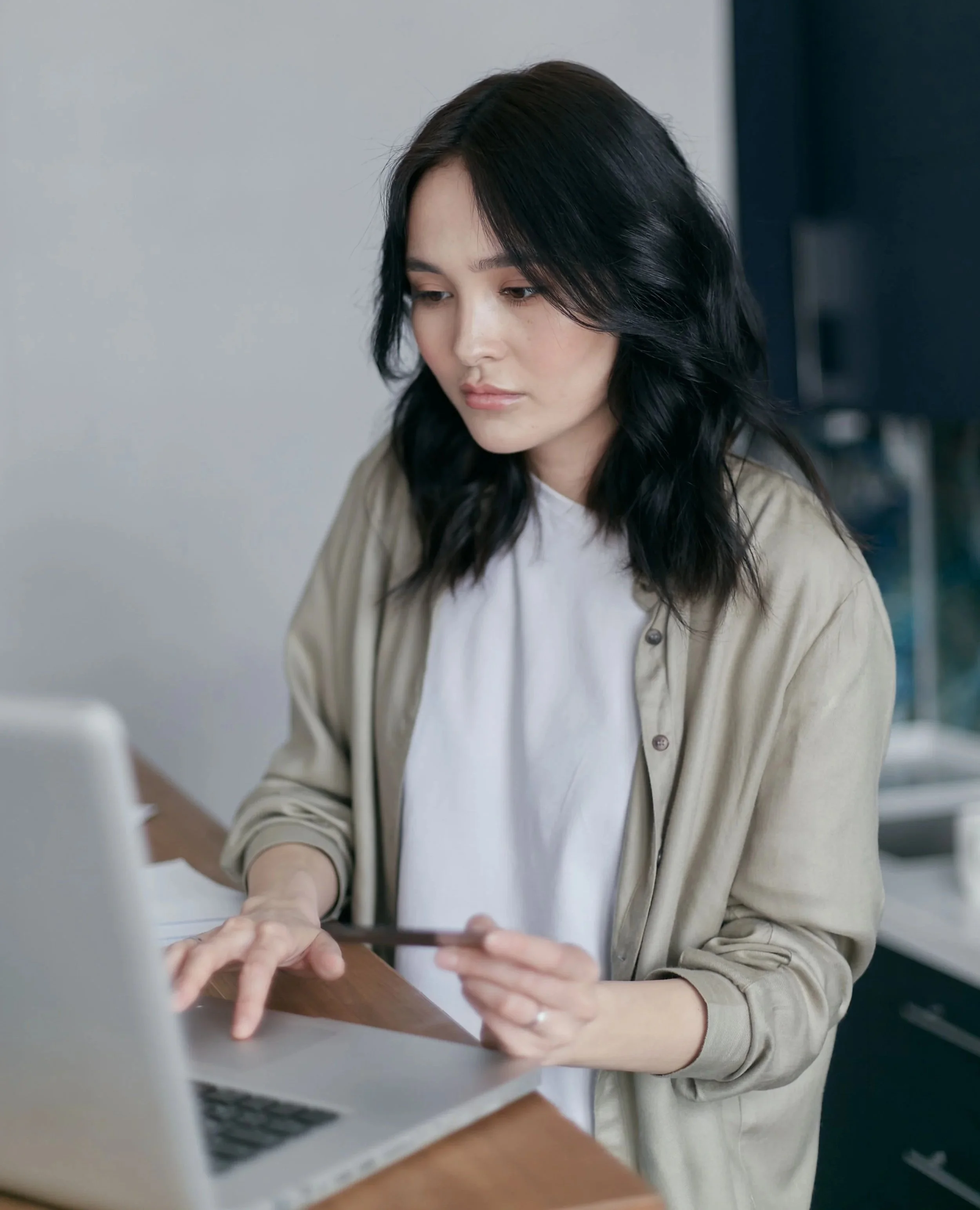 A woman with long black hair working on a laptop at a desk.