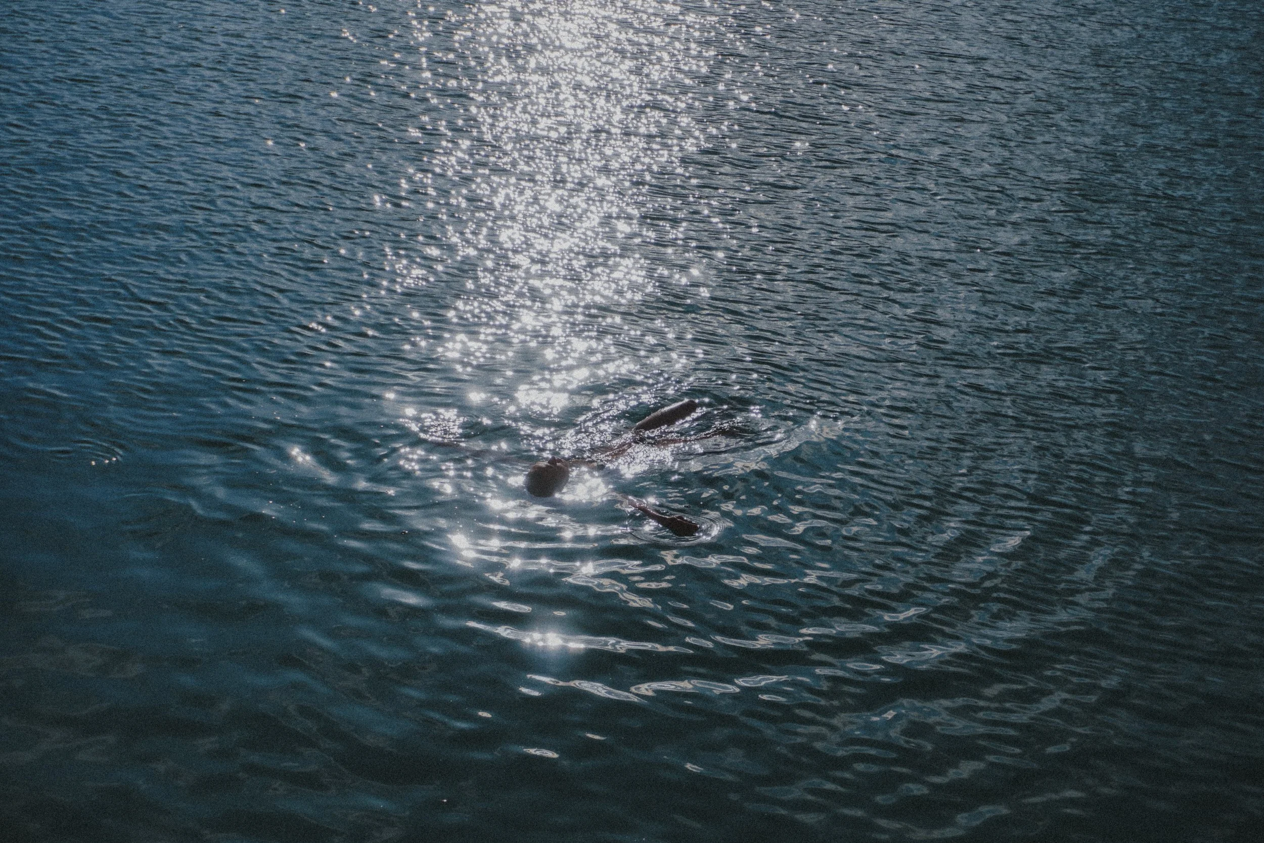 A person swimming in a body of water with sunlight reflecting off the surface.