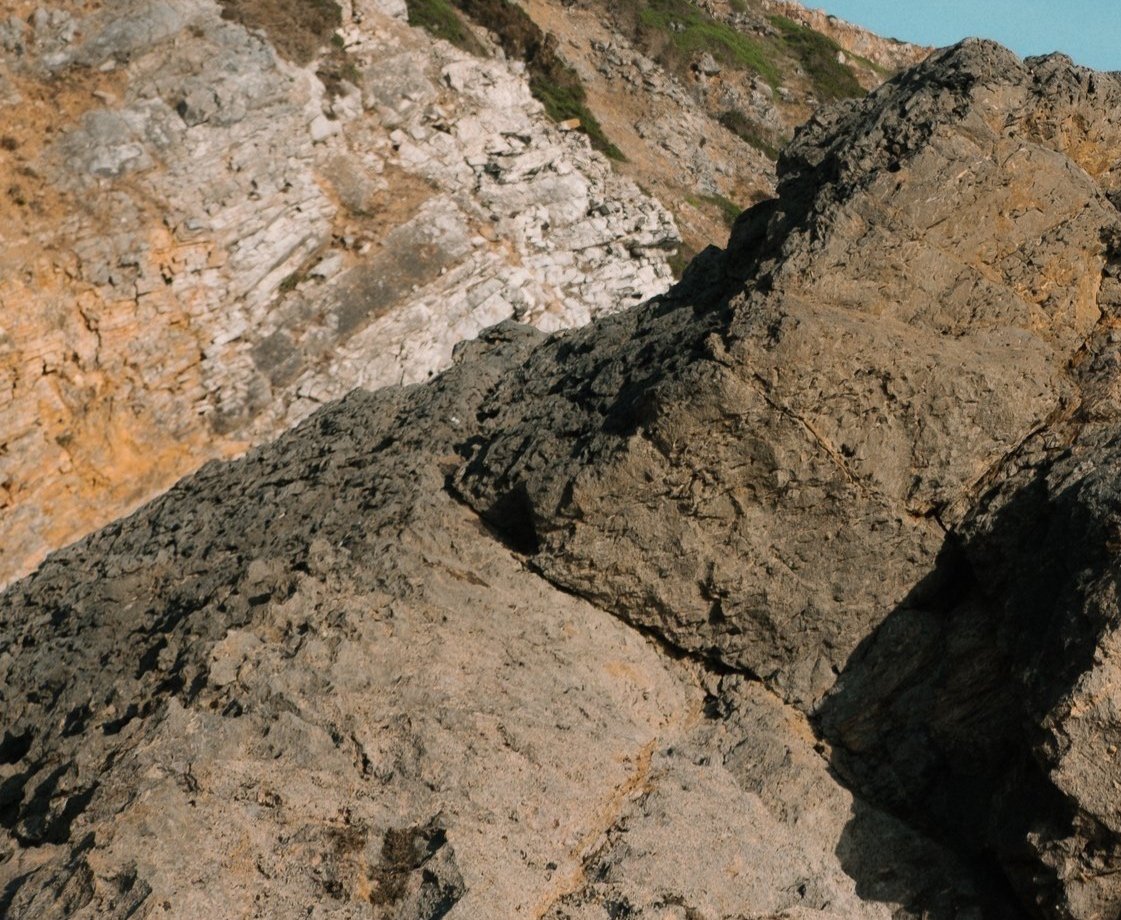 Close-up of large, textured rocks on a mountain slope with smaller rocks and distant cliffs in the background.