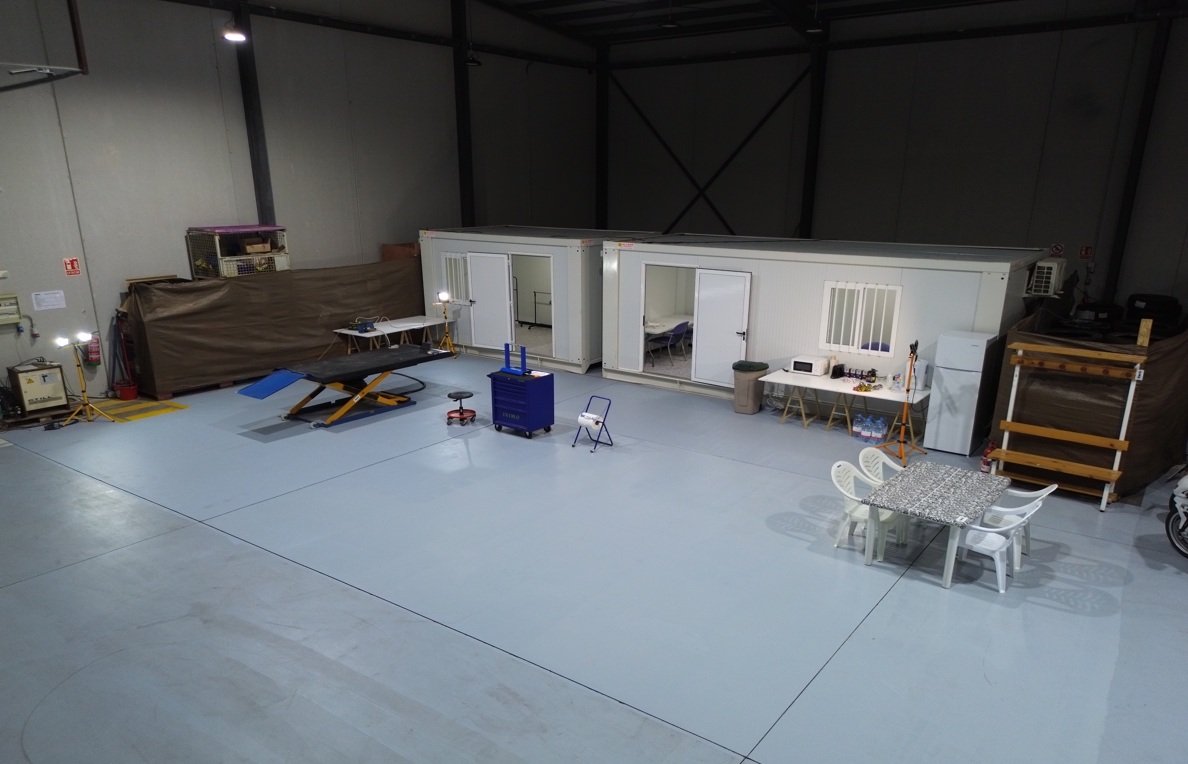 Indoor warehouse or training facility with modular rooms, tables, chairs, and equipment, including a dog agility ramp.
