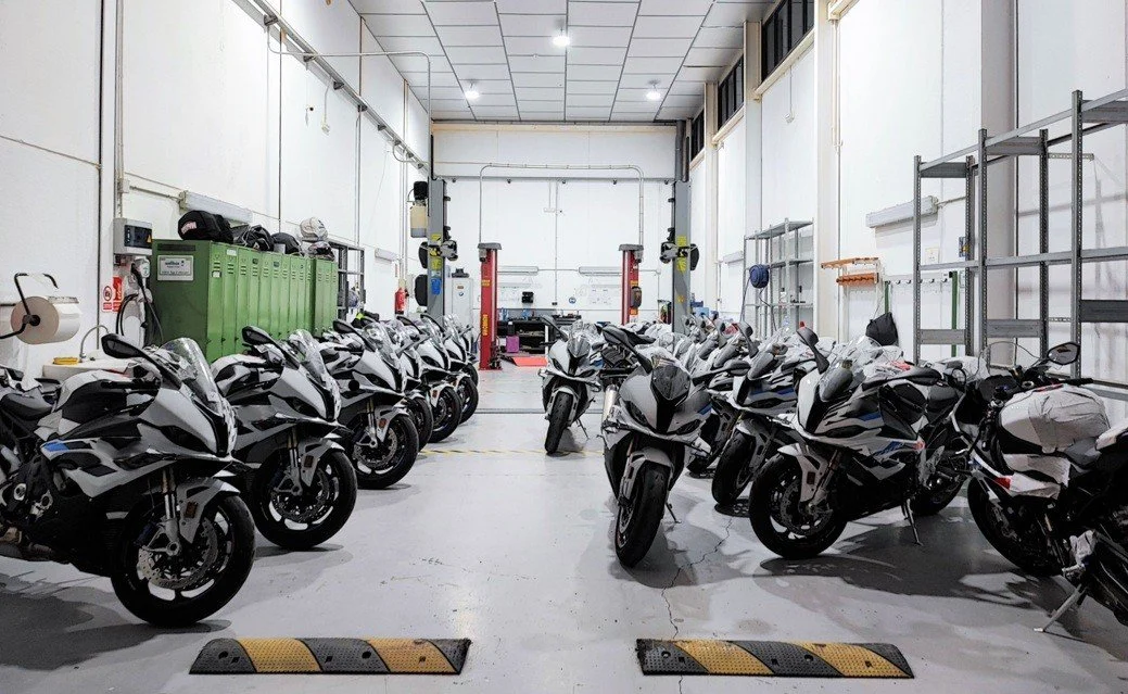 Indoor motorcycle parking garage with multiple white motorcycles parked in rows on either side of the aisle.