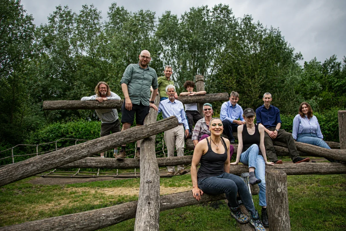 Group of people posing on a wooden playground structure outdoors with trees and a cloudy sky background.