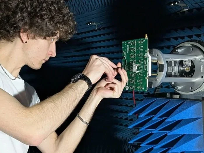 A person working on a green electronic circuit board inside an anechoic chamber.
